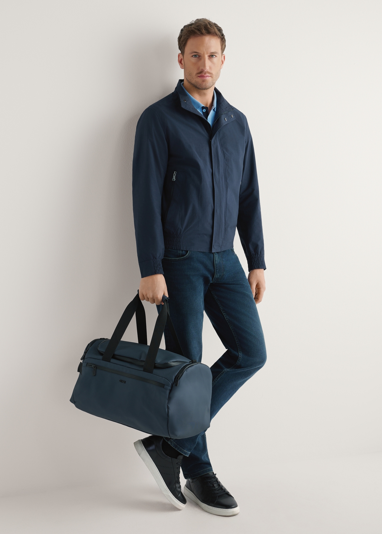 Námornícka modrá cestovná taška TORMN-0412-7D(W26) - pohľad na produkt, ktorú drží modelka, na svetlom pozadí. Viditeľné celé telo.