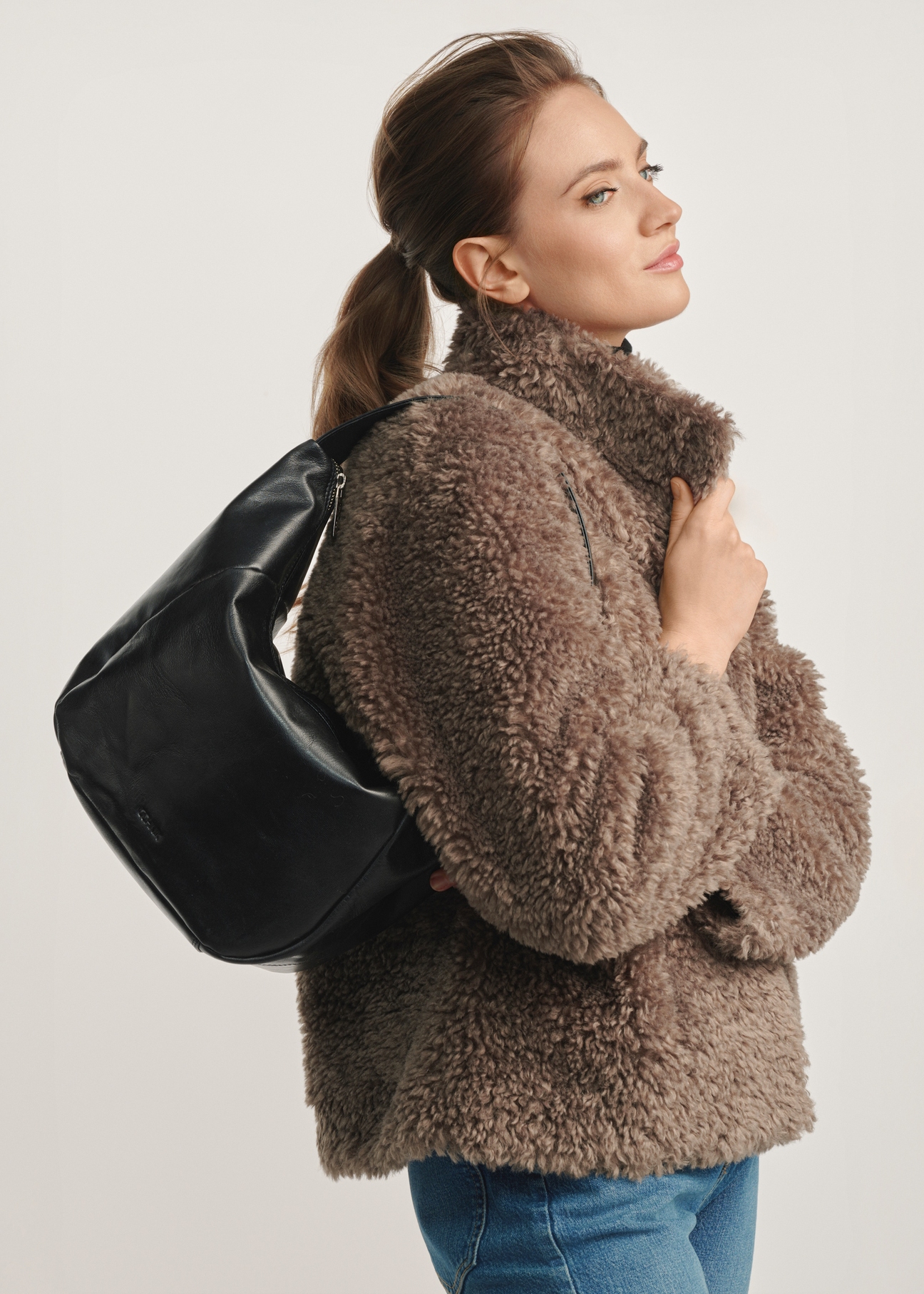 Čierna kožená kabelka hobo TORES-1135A-99(Z25) - pohľad spredu na produkt na modelke na bielom pozadí. Zboku viditeľná polovica siluety.