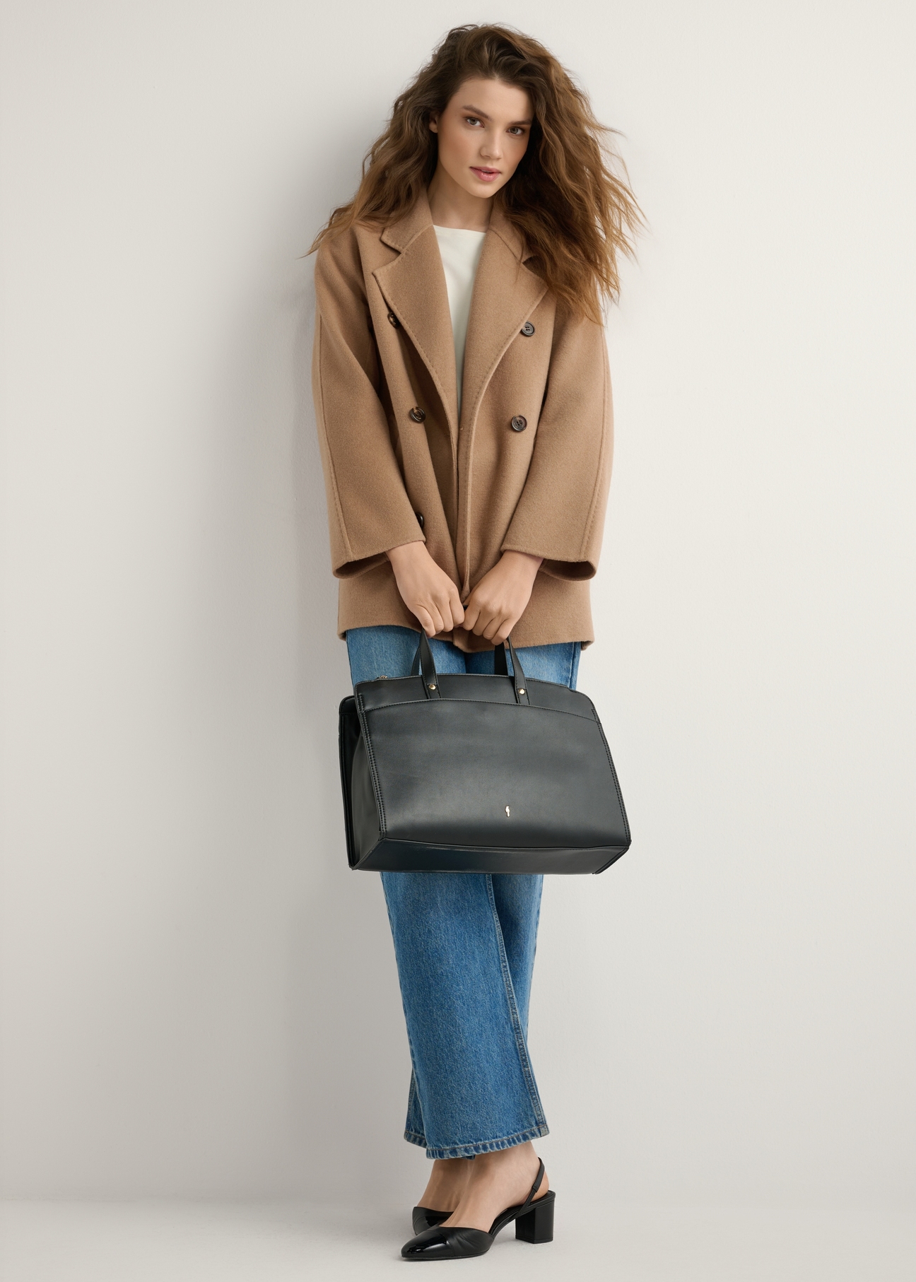 Čierna dámska koženková kabelka TOREC-1143-99(W26), pohľad na produkt v ruke modelky. Viditeľné celé telo.