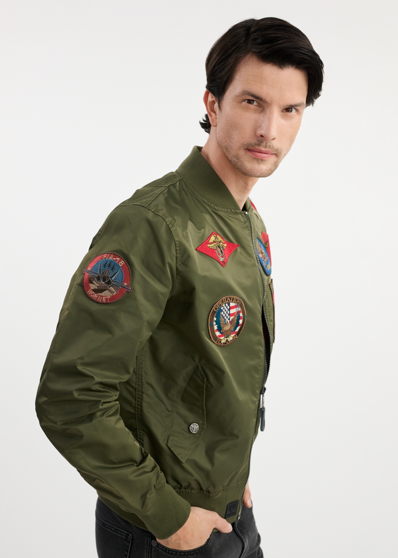 Pánska olivovozelená bomber bunda TOP GUN KURMT-0381-57(W25) - bočný pohľad na modelku na bielom pozadí. Viditeľná je polovica siluety.