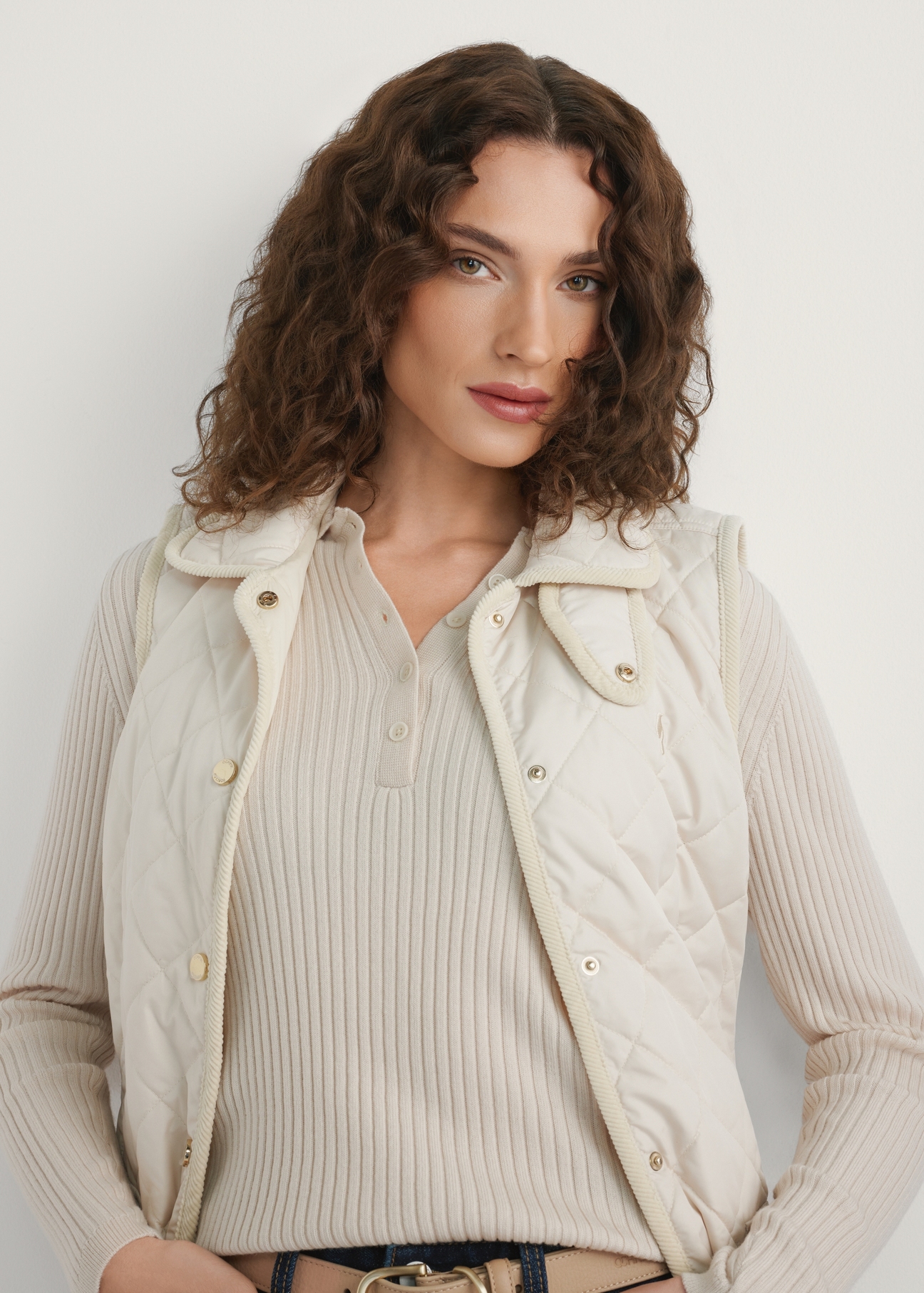 Svetlobéžová dámska prešívaná vesta KAMDT-0036-0B(W26) - pohľad spredu na výrobok, na modelke, na svetlom pozadí. Viditeľná polovica siluety.