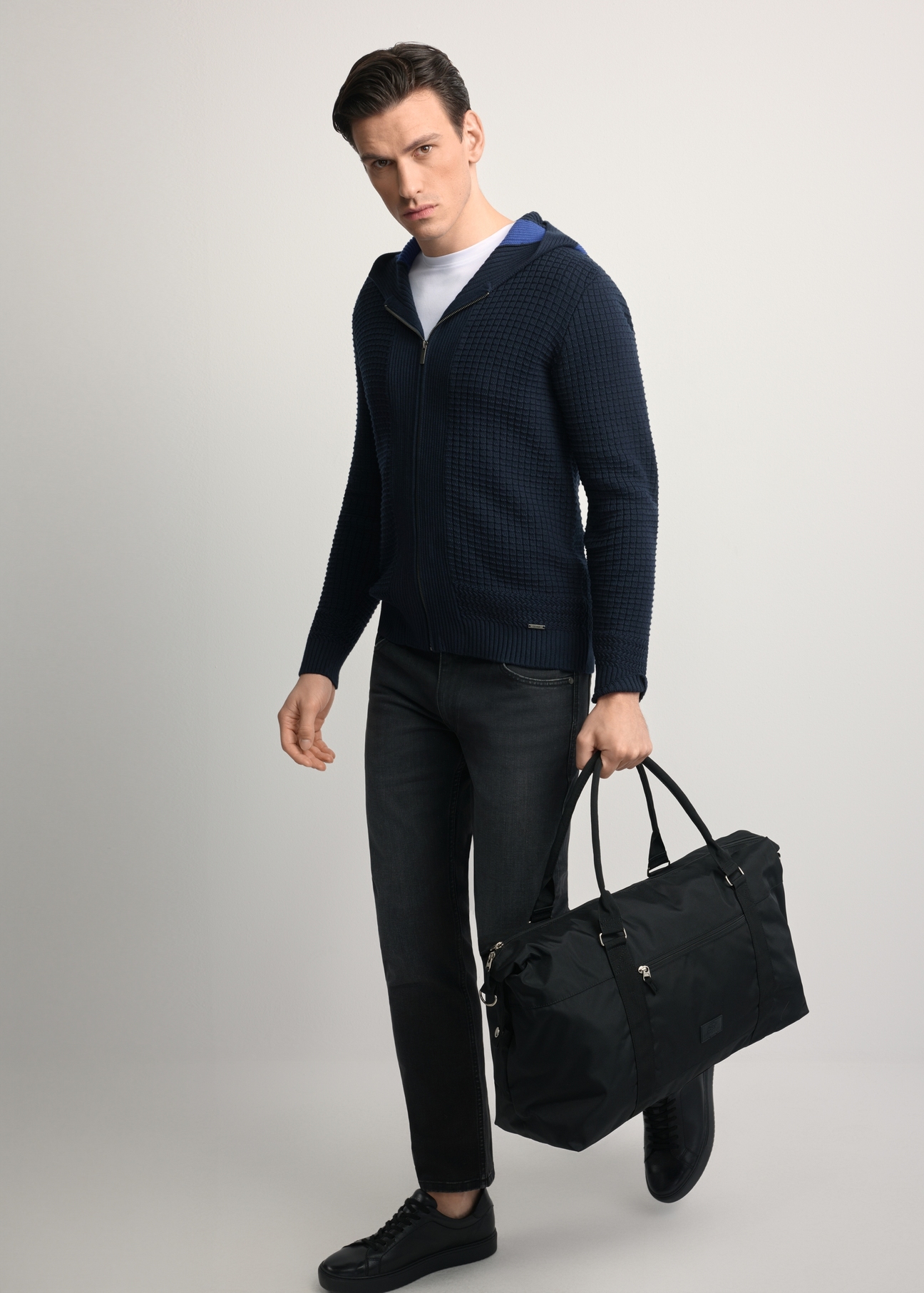 Čierna cestovná taška TORMN-0382-99(Z25) - diagonálny pohľad na produkt, ktorý drží modelka, na svetlom pozadí. Viditeľná je celá silueta.