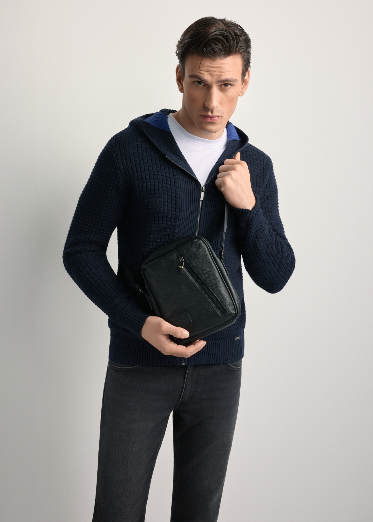 Čierna kožená pánska taška TORMS-0251B-99(Z25) - pohľad spredu na produkt, ktorý drží modelka, na svetlom pozadí. Viditeľná silueta po kolená.