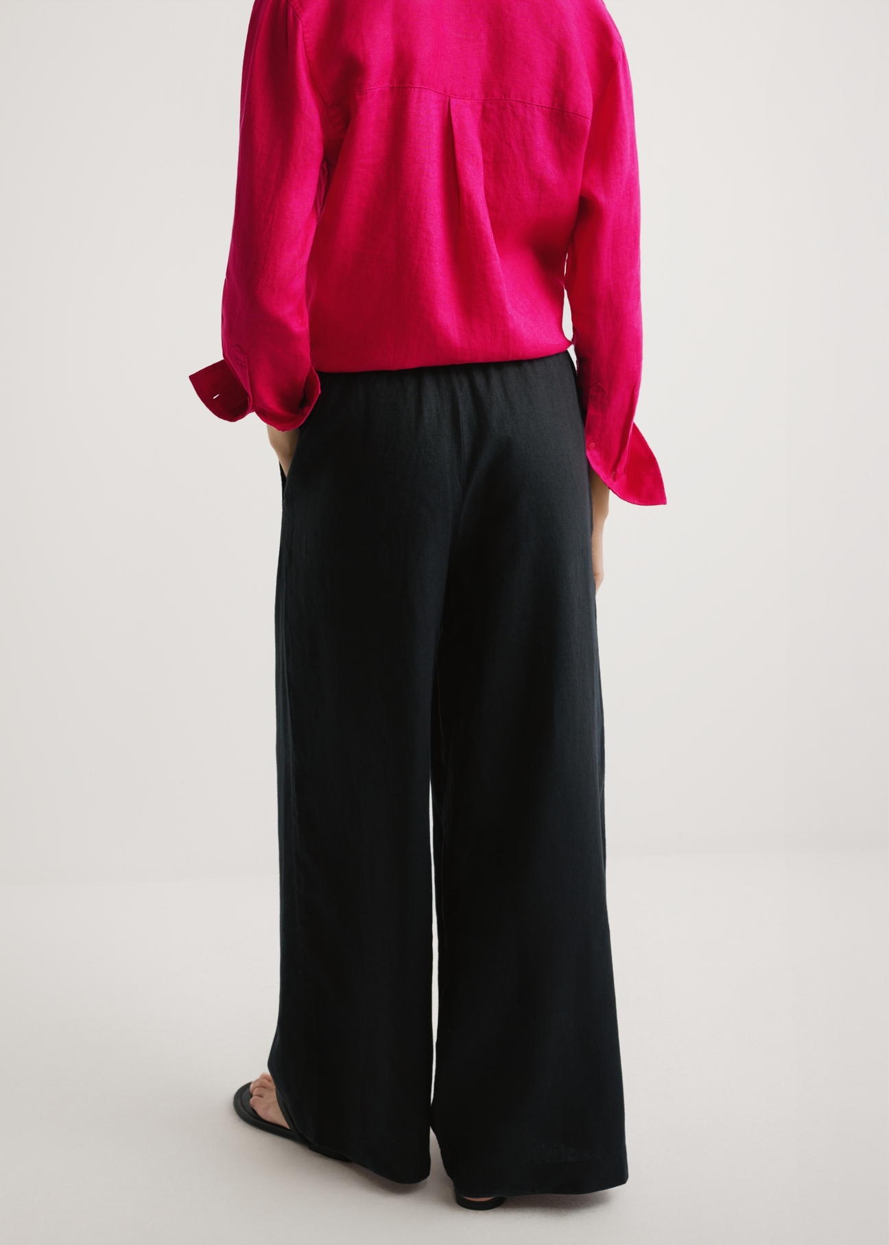 Dámske čierne ľanové nohavice SPODT-0124-99(W26) - pohľad na výrobok zozadu, na modelke, na svetlom pozadí. Viditeľná polovica siluety.