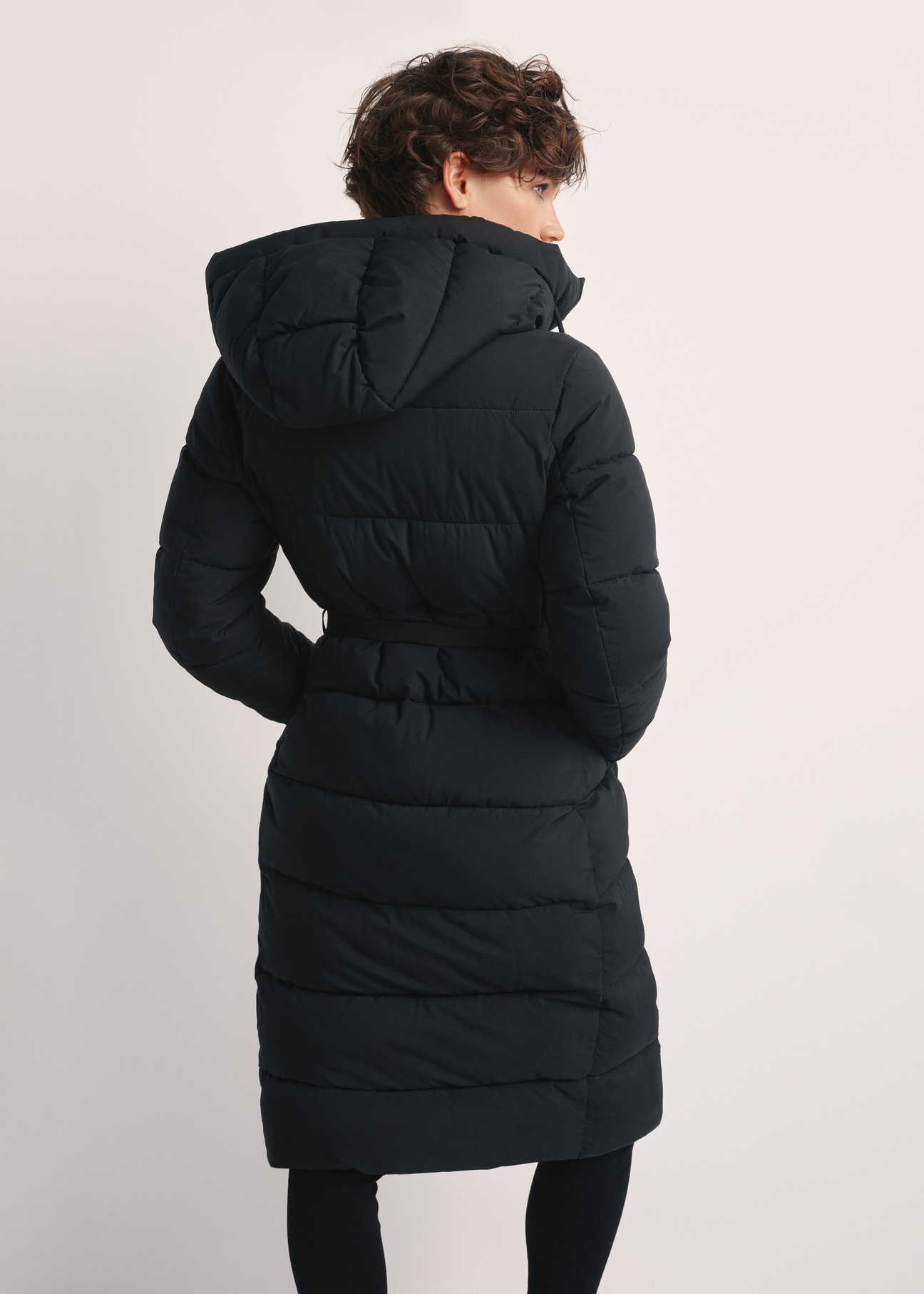 Dlhá čierna dámska bunda KURDT-0602-99(Z25), pohľad na produkt zozadu na modelke. Viditeľná polovica siluety.