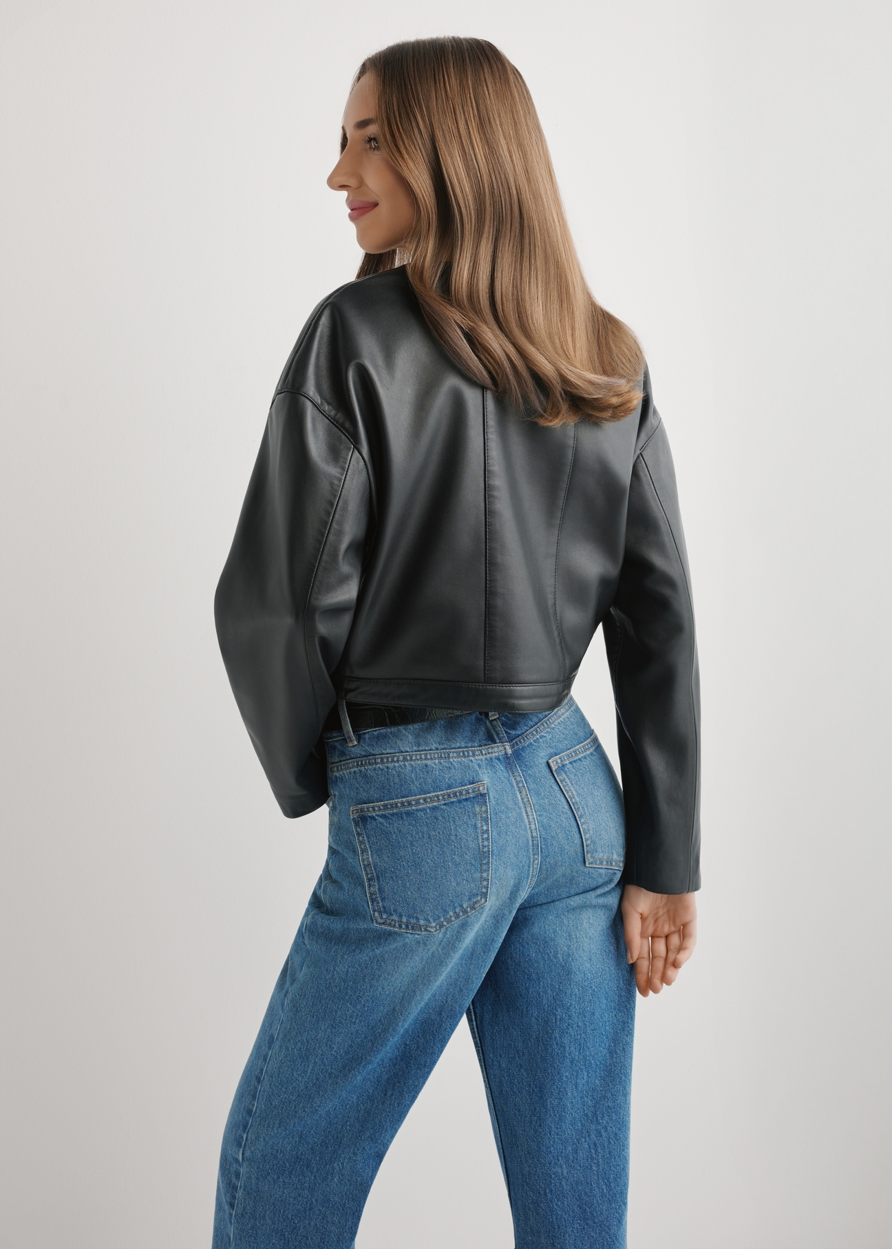 Dámska krátka čierna kožená bunda KURDS-0597-99(W26), pohľad na modelku zozadu. Viditeľná polovica siluety.