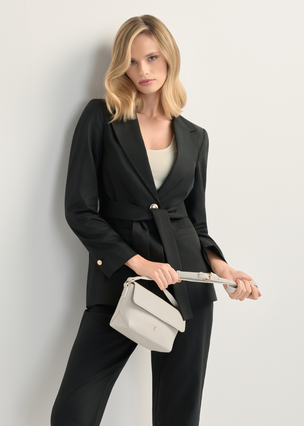 Krémová malá dámska kabelka cez rameno TOREC-0916-0B(W26), pohľad spredu na produkt v ruke modelky. Viditeľná polovica siluety.