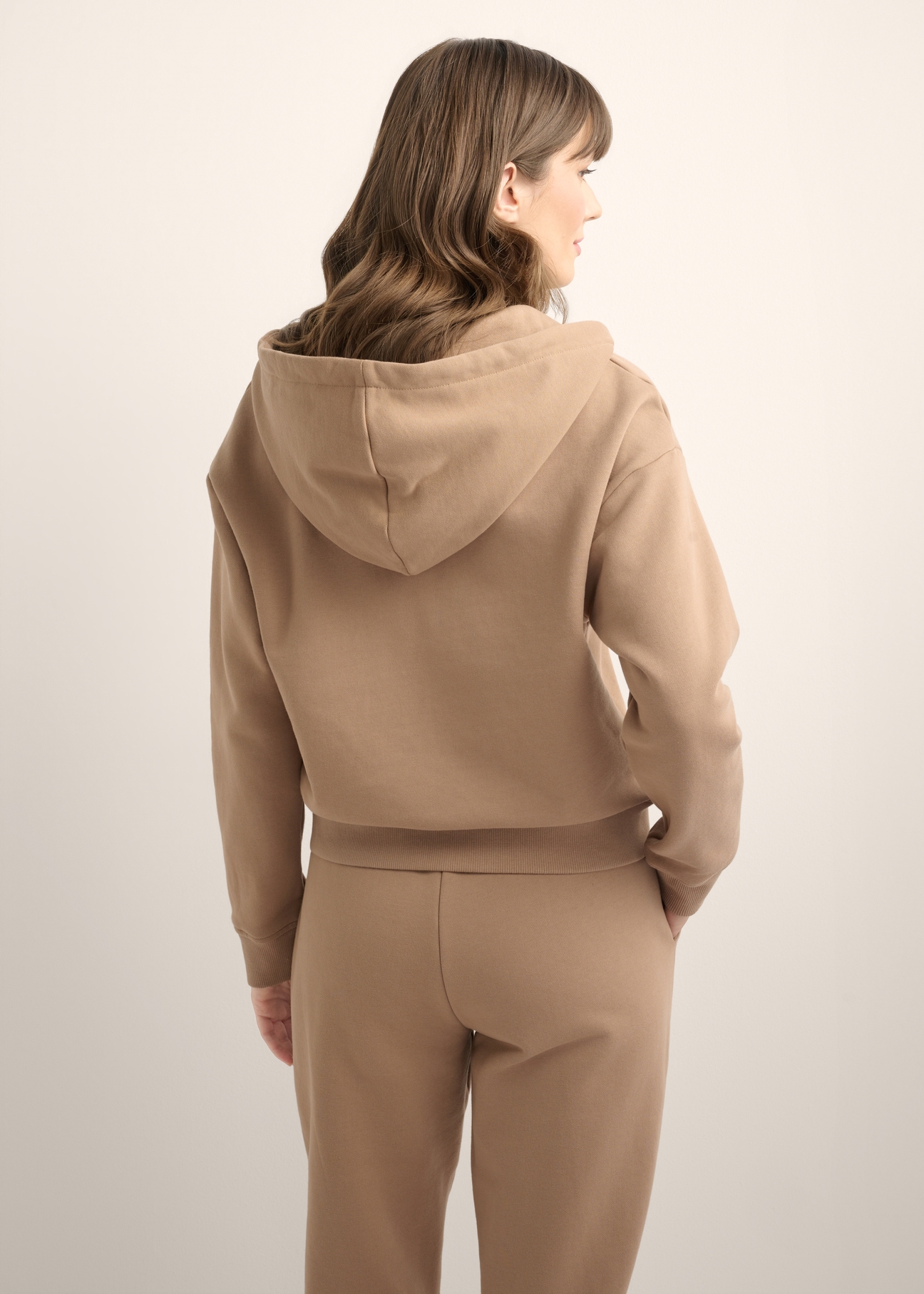 Dámska mikina s kapucňou na zips v ťavej farbe BLZDT-0122-1D(Z26), pohľad na produkt zozadu na modelke. Viditeľná polovica siluety.