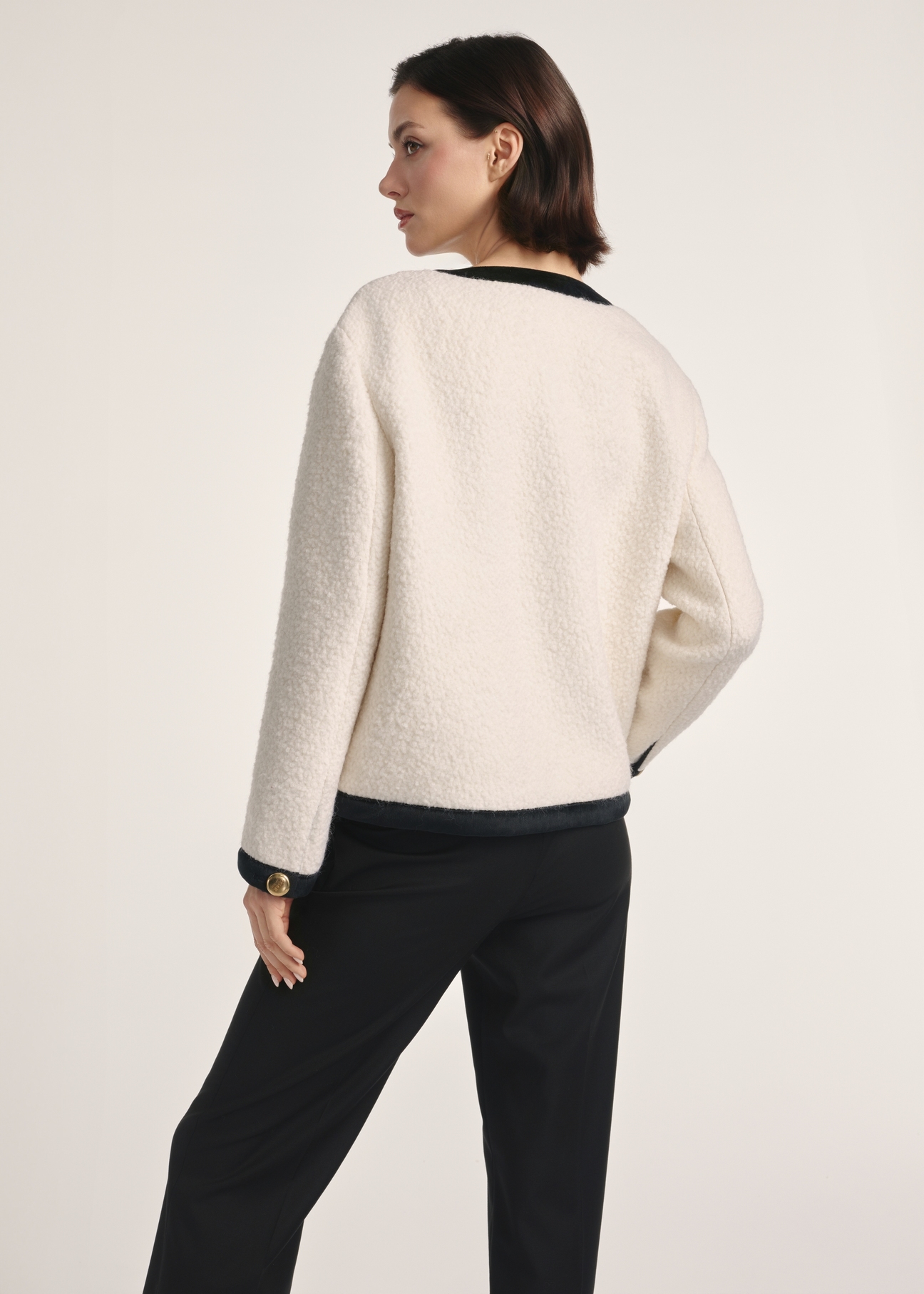 Krémová krátka dámska bunda s vlnou FUTDW-0037-12(Z25) - pohľad na produkt zozadu na modelke na bielom pozadí. Viditeľná silueta po kolená.