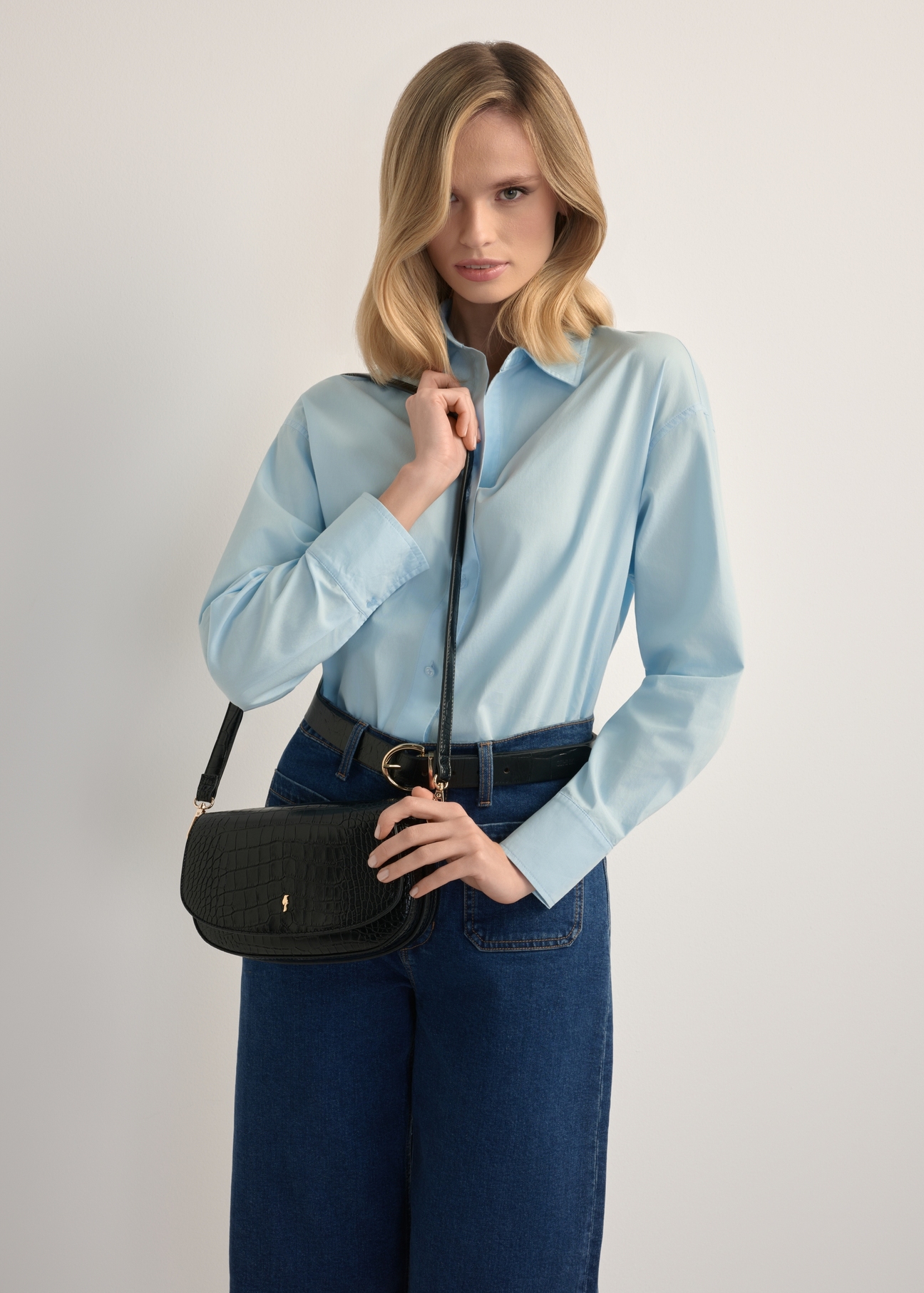 Malá čierna dámska kabelka cez rameno z krokodílej kože TOREC-1185-9G(W26), pohľad na produkt na ramene modelky. Viditeľná polovičná silueta.