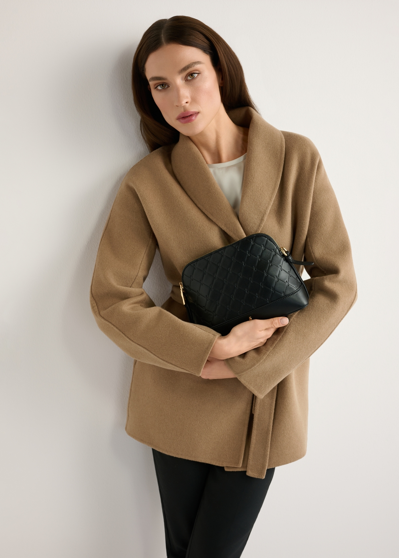 Čierna dámska kabelka s monogramom TOREC-1180-9P(W26), pohľad na produkt v rukách modelky. Viditeľná polovica siluety.