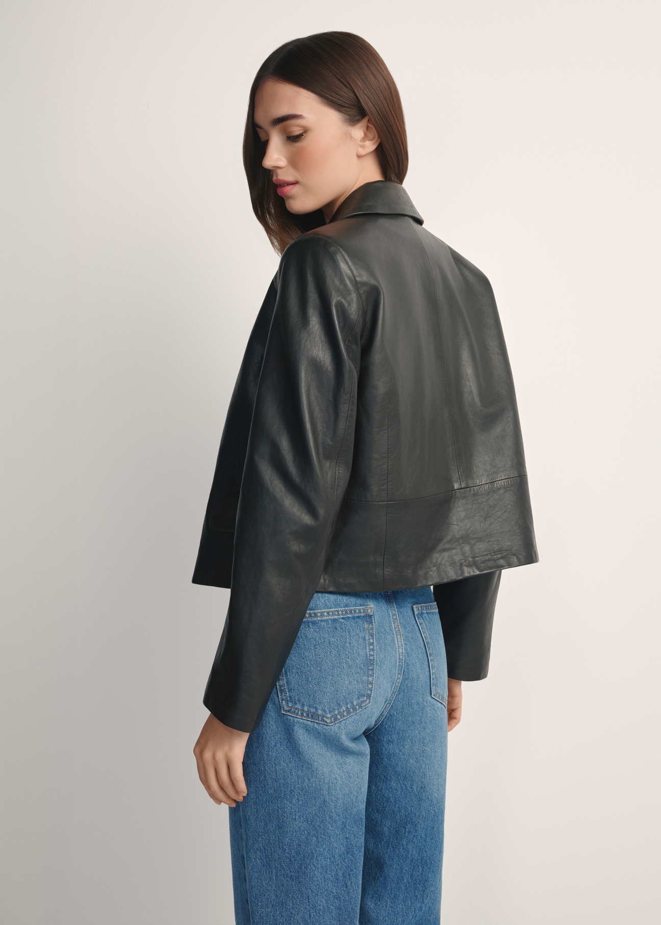 Čierna krátka dámska kožená bunda KURDS-0598-99(W26), pohľad na produkt zozadu na modelke, viditeľná polovica siluety.