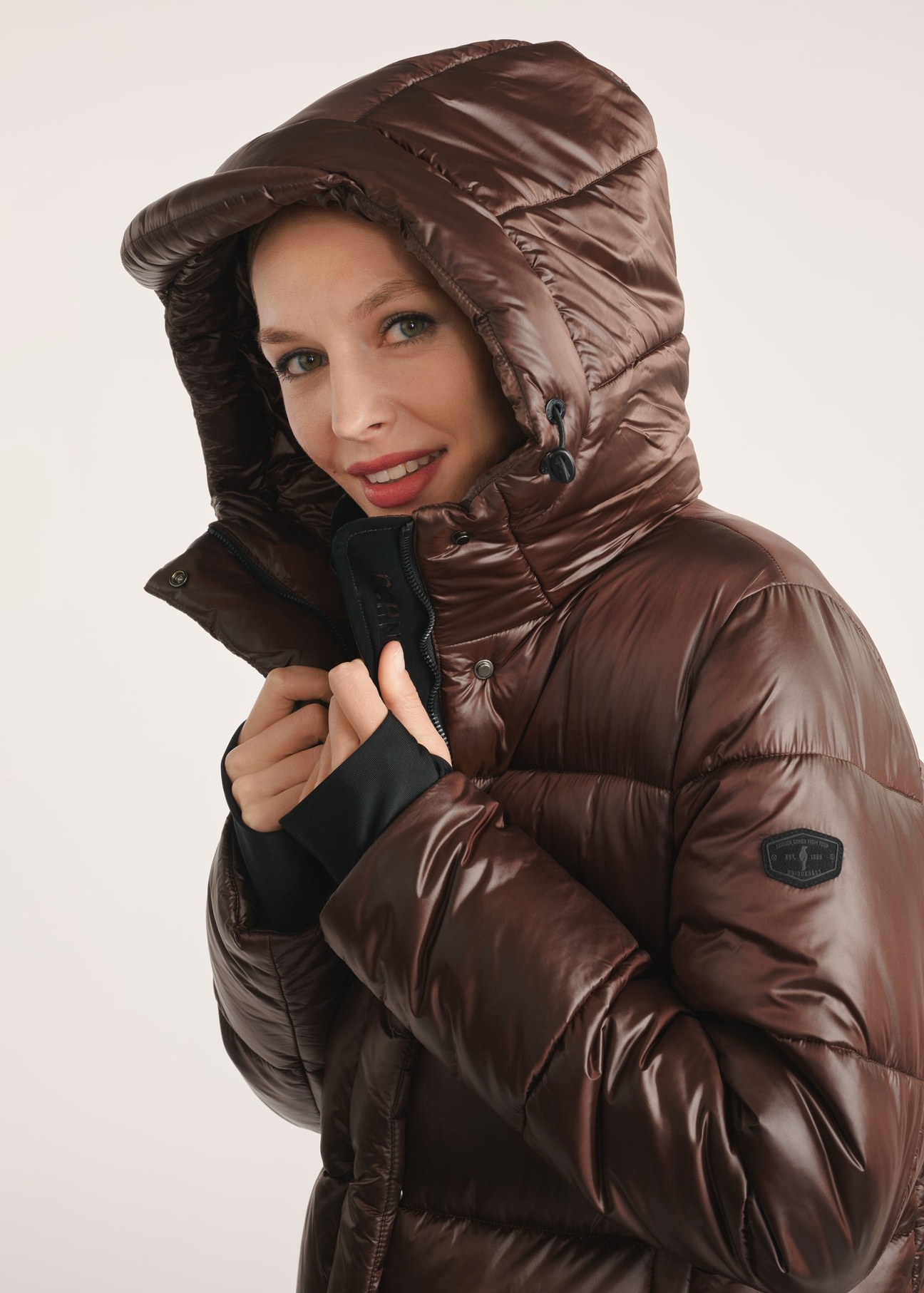Hnedá dlhá dámska zimná bunda KURDT-0531-1H(Z26)- detailný záber na modelku na bielom pozadí. Viditeľná polovica siluety.