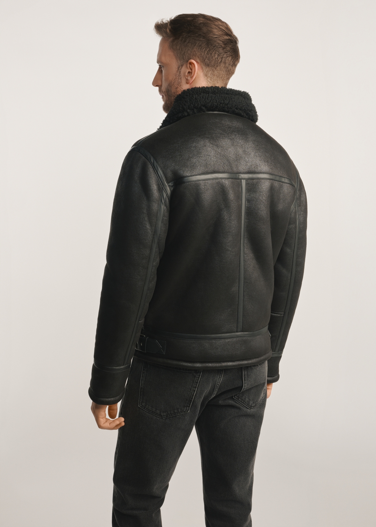 Klassischer schwarzer Herren-Lammfellmantel KOZMP-0001A-99(Z24), Produkt von hinten am Model sichtbar, die Hälfte der Silhouette sichtbar.