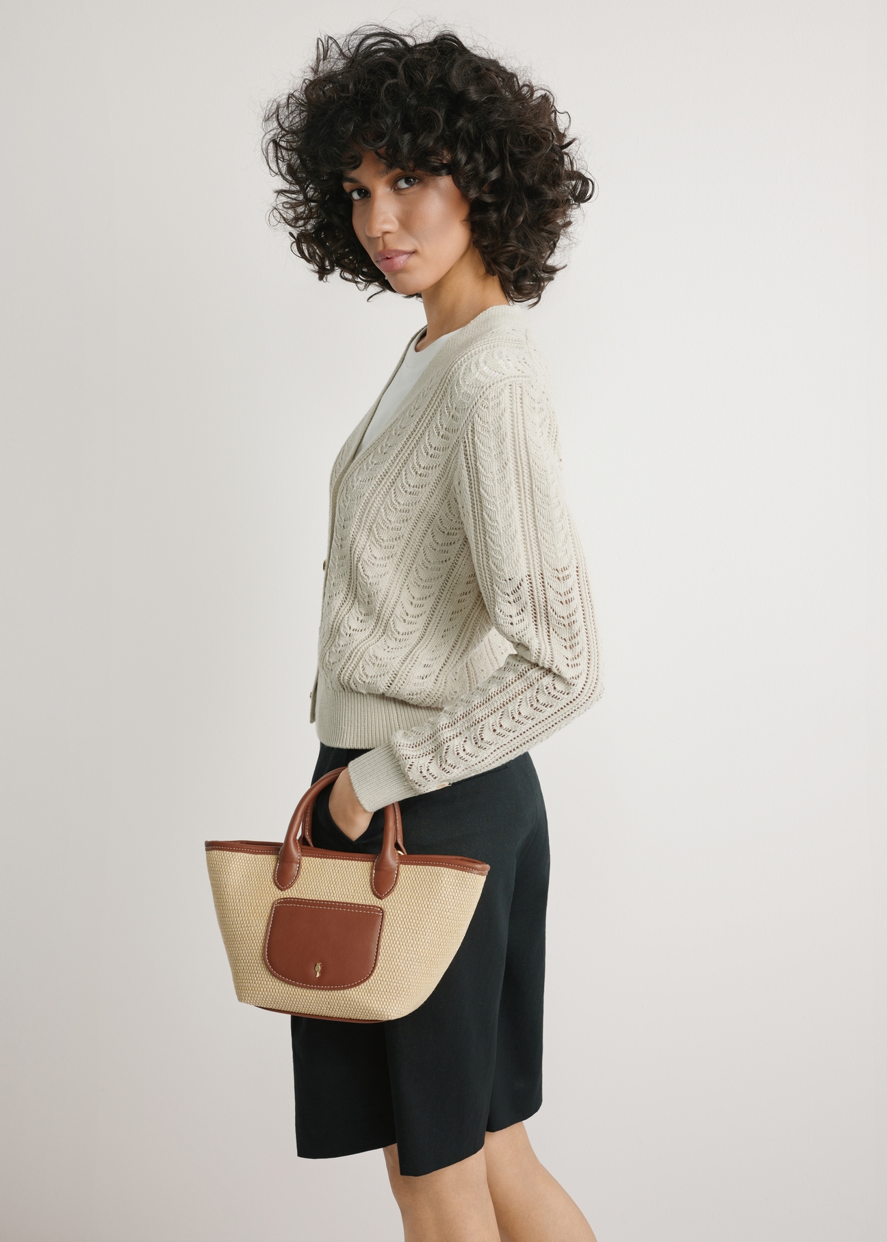 Malá tkaná dámska kabelka TOREC-1230-1B(W26) - pohľad spredu na produkt, ktorý drží modelka, na svetlom pozadí. Viditeľná je silueta po pás.