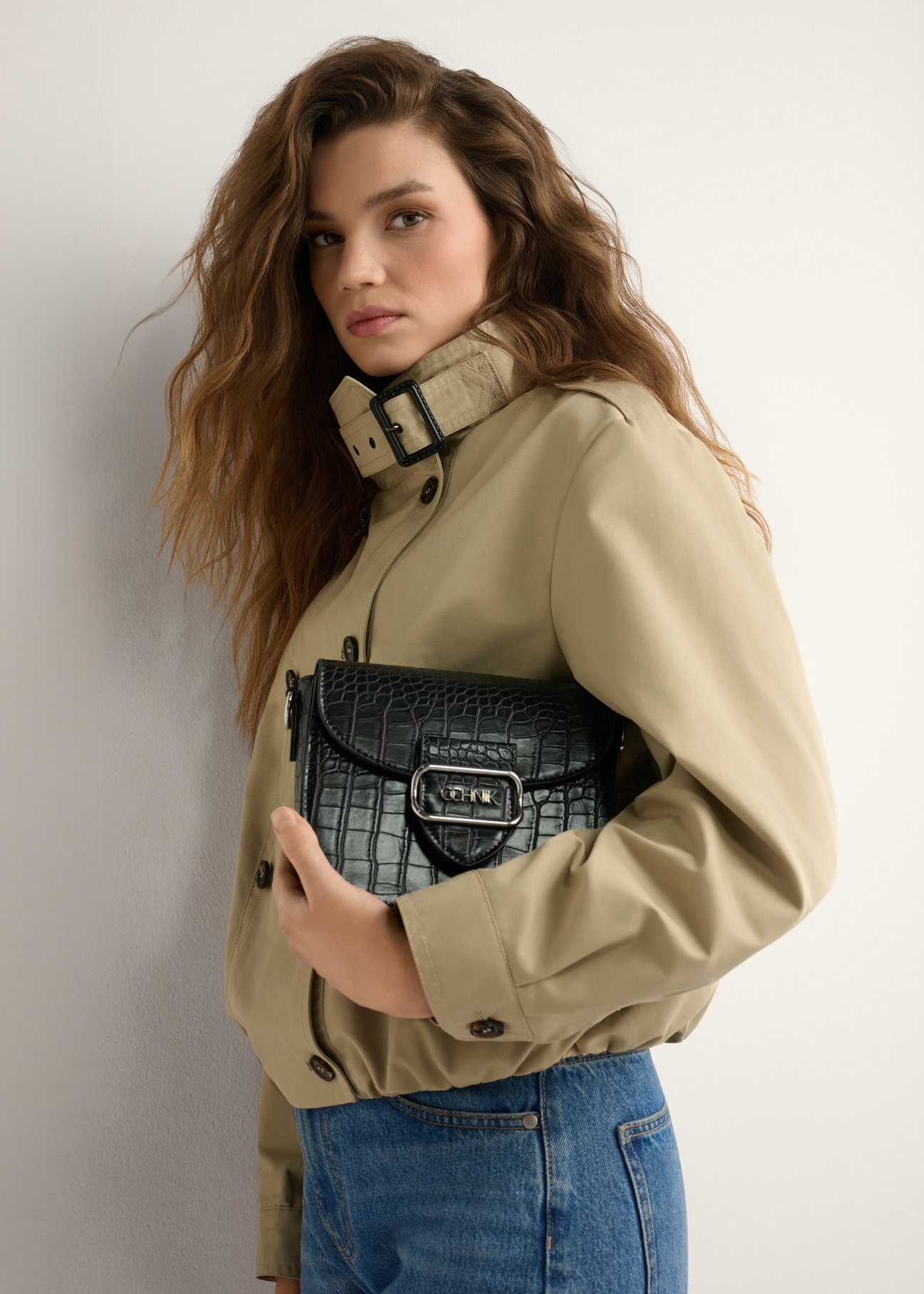 Dámska čierna krokodília kabelka cez rameno TOREC-0880-9G(W26) - pohľad spredu na produkt, ktorý drží modelka, na svetlom pozadí. Viditeľná je polovica siluety.