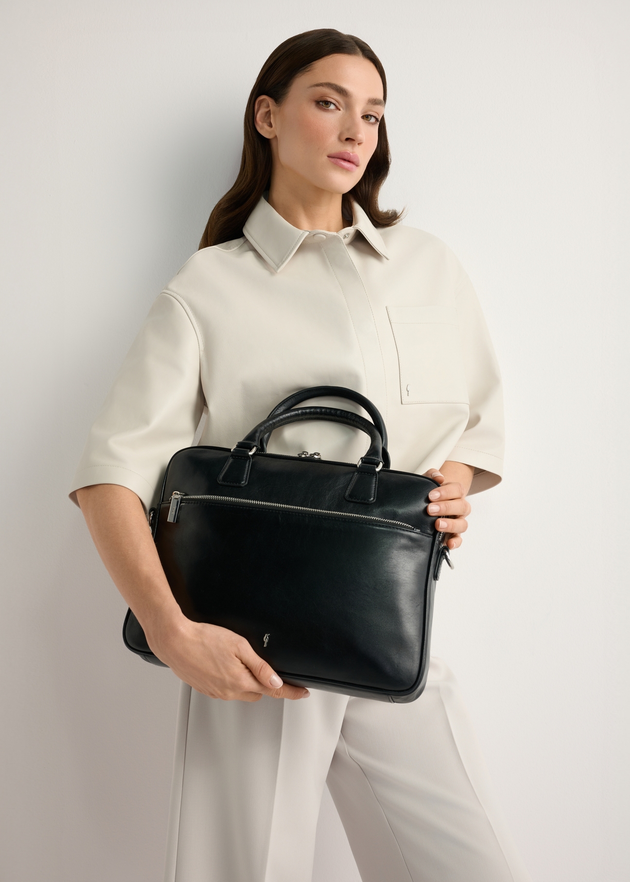 Čierna kožená taška na notebook TORES-1227-99(W26), pohľad na produkt v rukách modelky. Viditeľná polovica siluety.