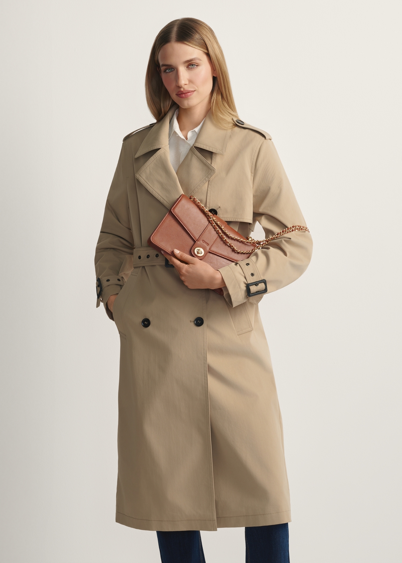 Dámska hnedá taška cez rameno TOREC-1137-1F(W26) - pohľad spredu na produkt, na modelke, na svetlom pozadí. Viditeľná silueta po kolená.