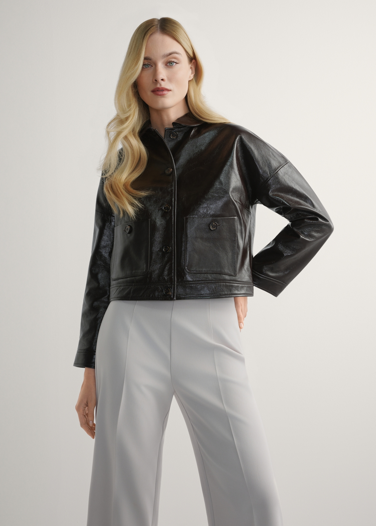 Dámska hnedá krátka kožená bunda KURDS-0593-1I(W26) - pohľad spredu na výrobok, na modelke, na svetlom pozadí. Viditeľná silueta po kolená.