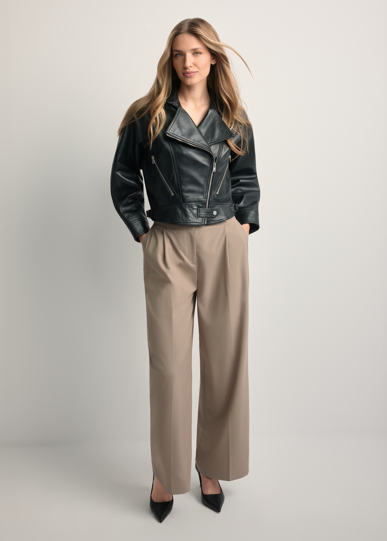 Dámska krátka čierna kožená bunda KURDS-0607-99(W26) - pohľad spredu na produkt na modelke, na svetlom pozadí. Viditeľné celé telo.