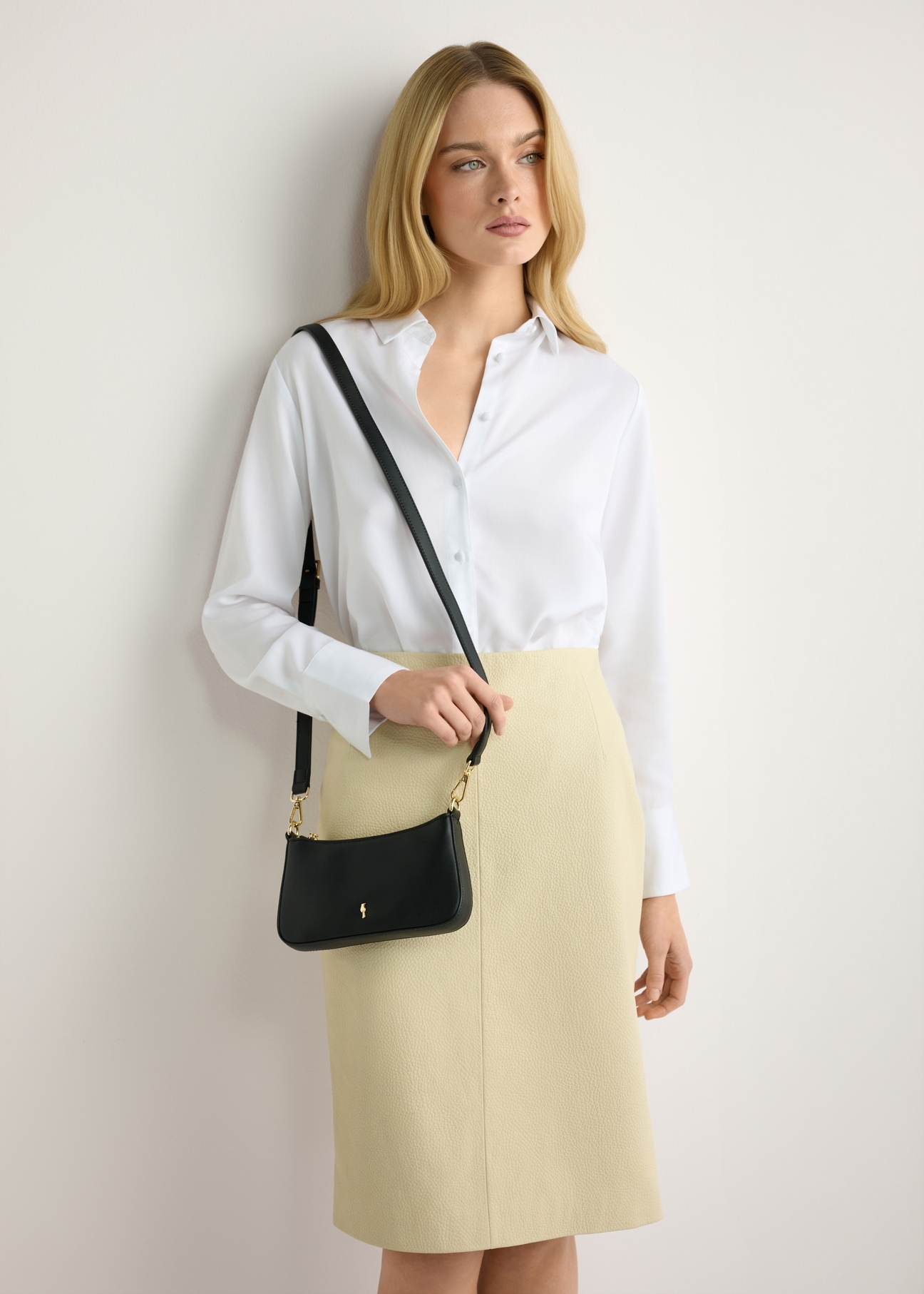 Malá čierna dámska kabelka TOREC-1188-99(W26) - pohľad spredu na produkt, na modelke, na svetlom pozadí. Viditeľná silueta po polovičnú dĺžku.