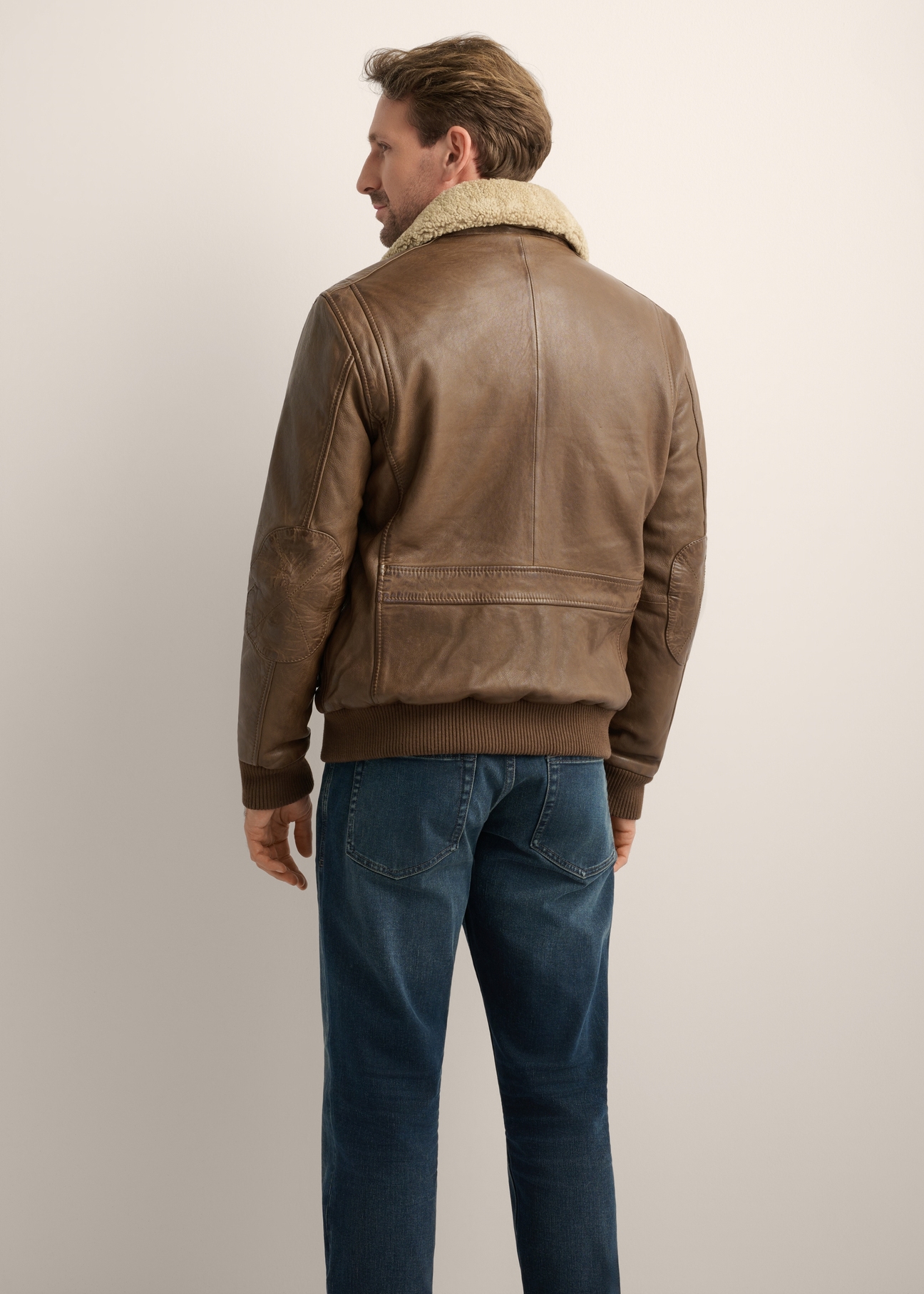 Pánska hnedá kožená bomber bunda KURMS-0424-1K(Z26), pohľad na produkt zozadu na modeli. Viditeľná polovica siluety.
