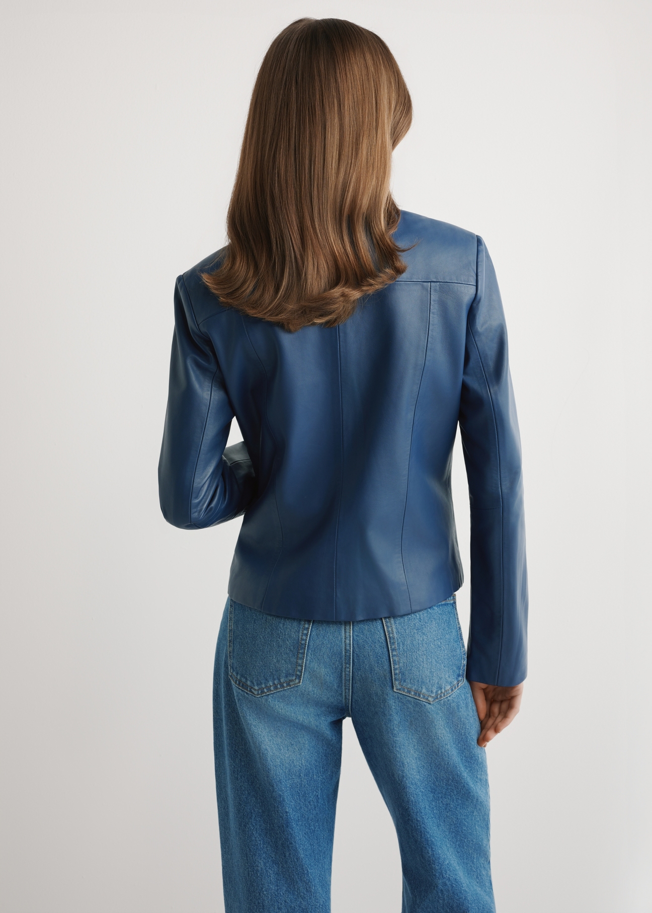 Dámska kožená bunda v tmavomodrej farbe KURDS-0532-7D(W26) - pohľad na výrobok zozadu, na modelke, na svetlom pozadí. Viditeľná polovica siluety.
