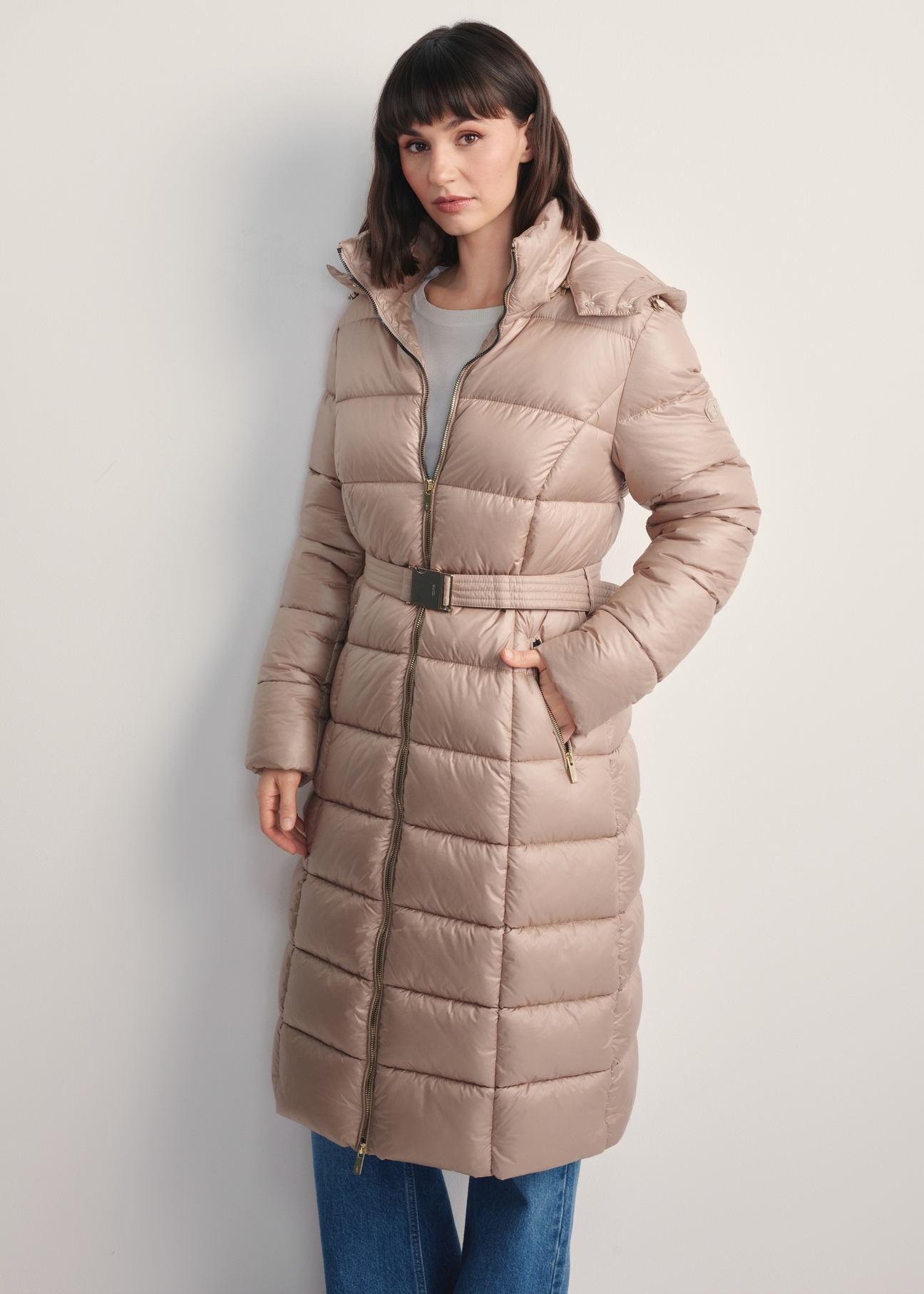 Béžová dámska dlhá bunda KURDT-0603-82(Z25), pohľad spredu na produkt na modelke. Viditeľná polovica siluety.