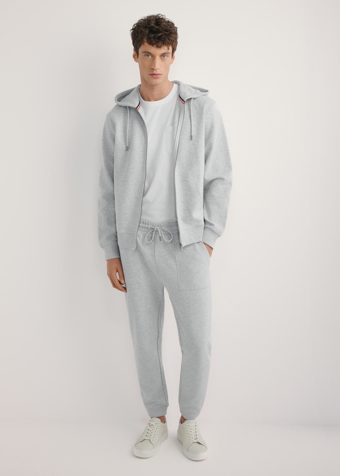 Pánska sivá mikina s kapucňou BLZMT-0079-9A(W26), pohľad spredu na modelku. Viditeľné celé telo.