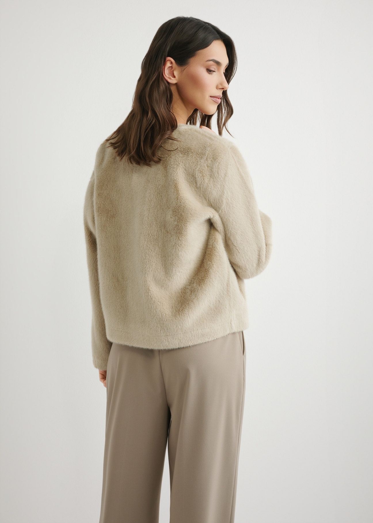 Dámsky krátky béžový kožuch FUTDP-0079-1A(W26), pohľad na modelku zozadu. Viditeľná polovica siluety.