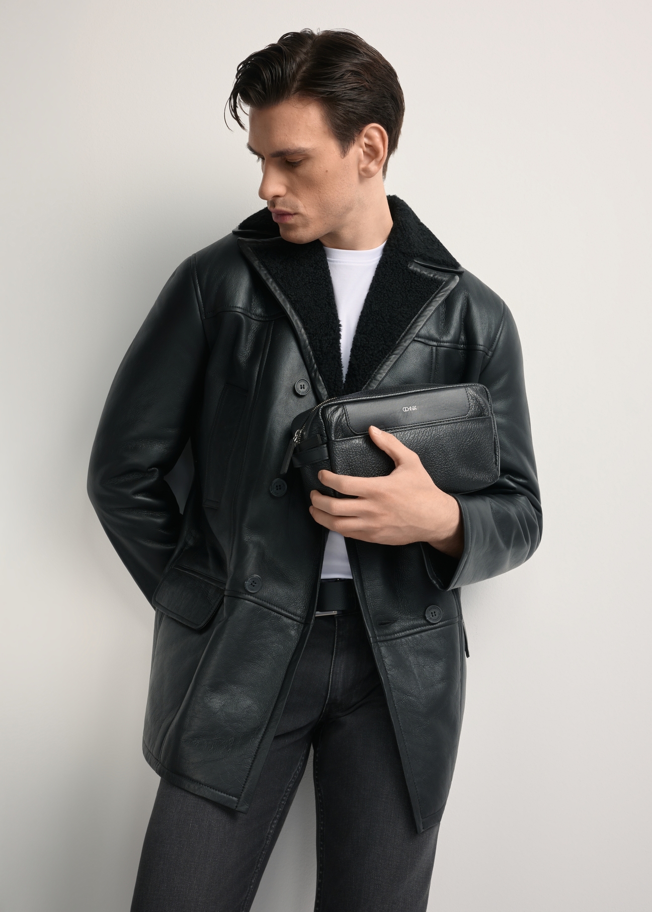 Pánska kožená kozmetická taška s logom TORMS-0298A-99(Z25) - diagonálny pohľad na produkt, ktorý drží modelka, na bielom pozadí. Viditeľná silueta po kolená.