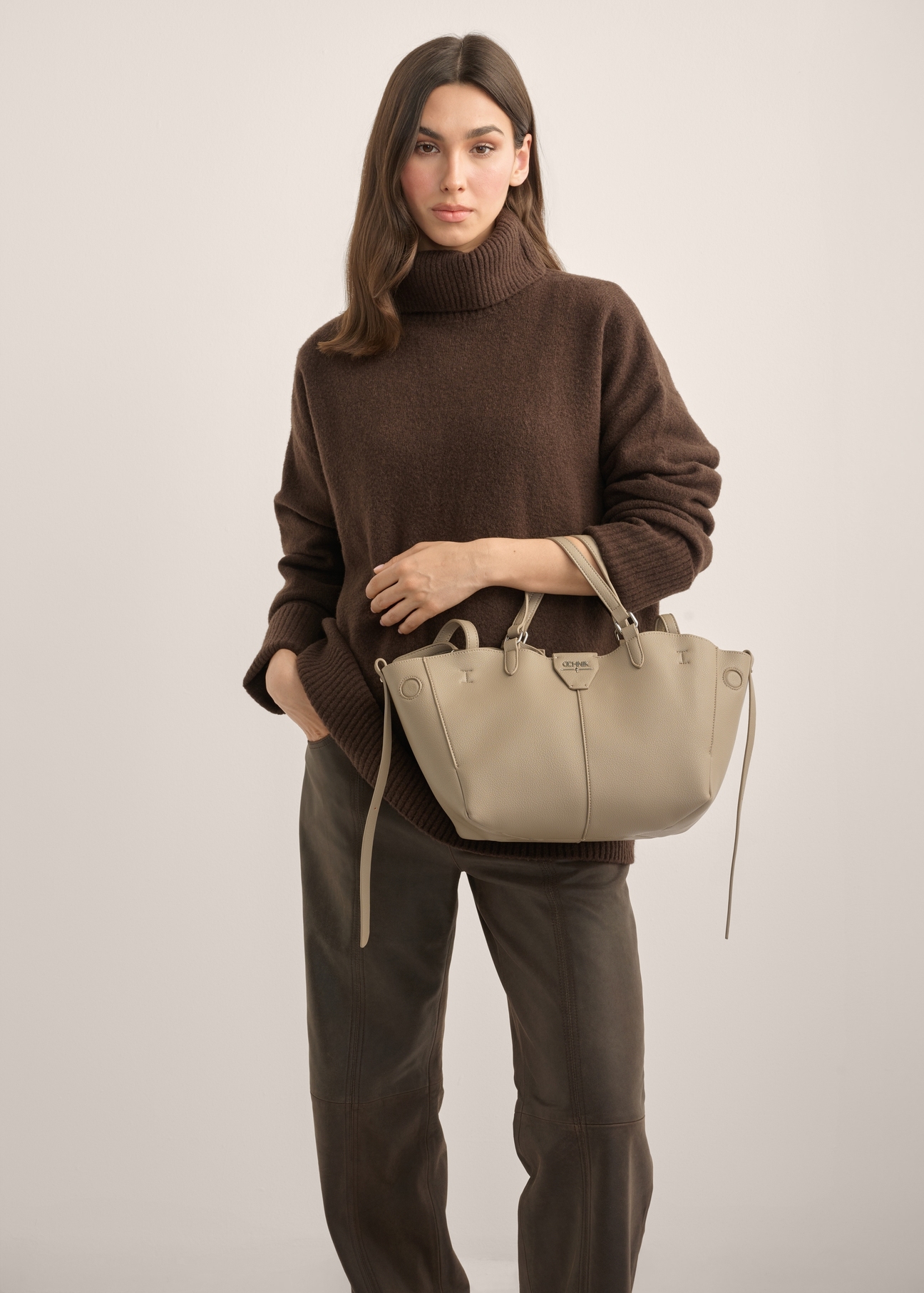 Dunkelbeige Damenhandtasche TOREC-1231-1K(Z26). Produktansicht von vorn an einem Model, die Silhouette ist zur Hälfte sichtbar.