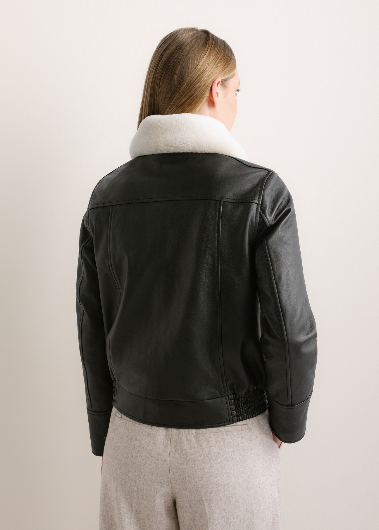 Čierna kožená bomber bunda KURDS-0646-99(Z26), pohľad zozadu na produkt na modelke. Viditeľná polovica siluety.