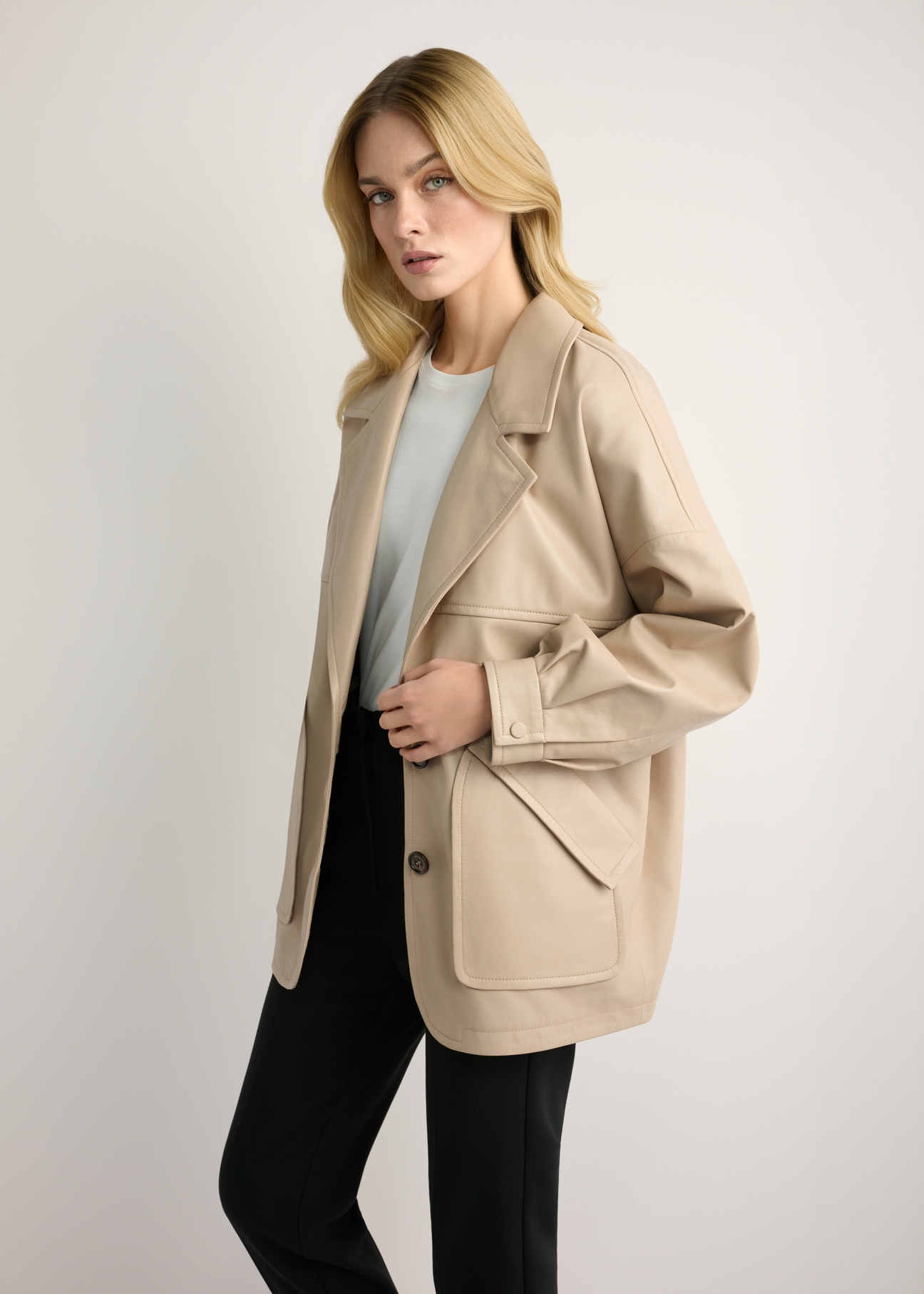 Dámska béžová kožená bunda oversize KURDS-0577-1B(W26) - bočný pohľad na produkt, na modelke, na svetlom pozadí. Viditeľná silueta po kolená.