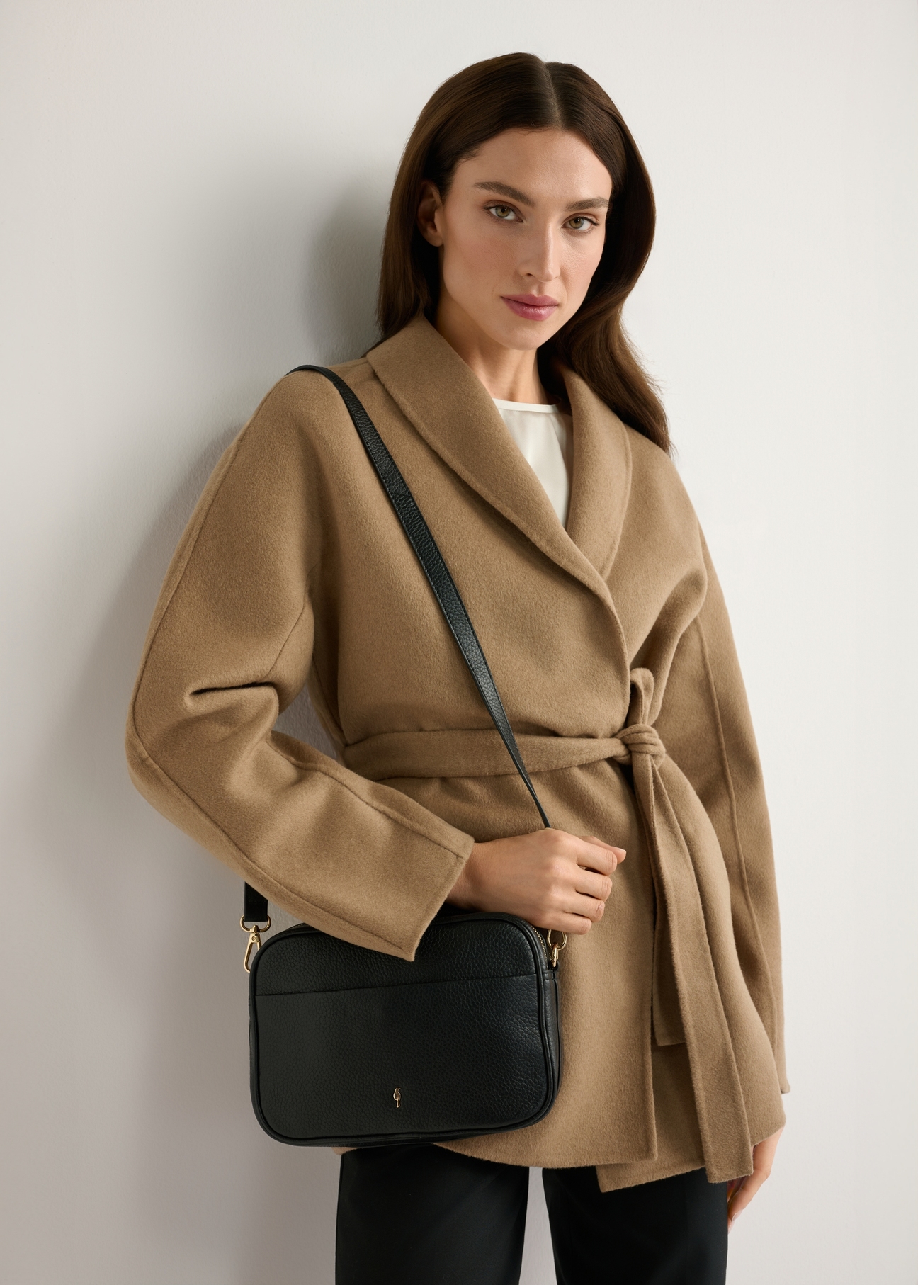 Malá čierna kožená dámska kabelka TORES-1284-9I(W26) - pohľad spredu na produkt, na modelke, na svetlom pozadí. Viditeľná silueta po polovičnú dĺžku.