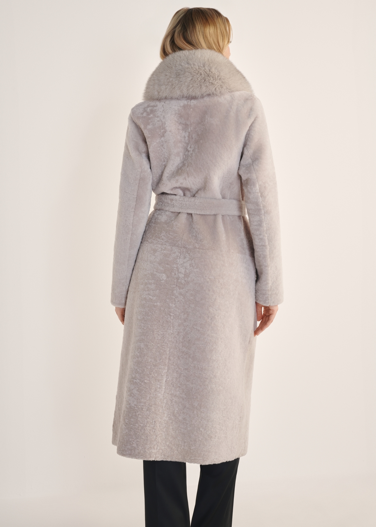 Svetlobéžový obojstranný dlhý dámsky kabát z ovčej kože KOZDS-0089-3037(Z25) - pohľad na výrobok zozadu na bielom podklade. Viditeľné celé telo.