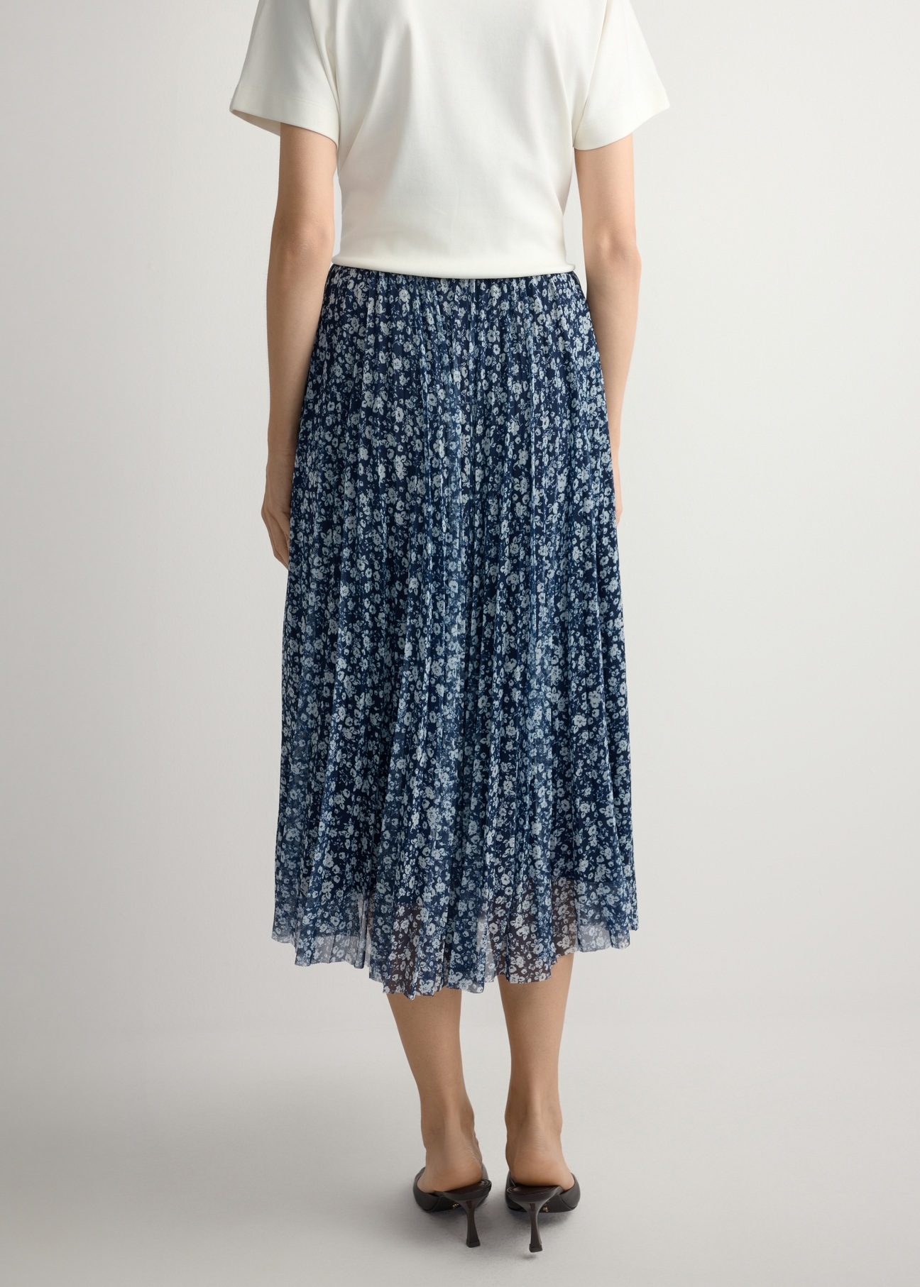 Kvetinová skladaná midi sukňa SPCDT-0110-7P(W26), pohľad zozadu na produkt na modelke. Viditeľná polovica siluety.