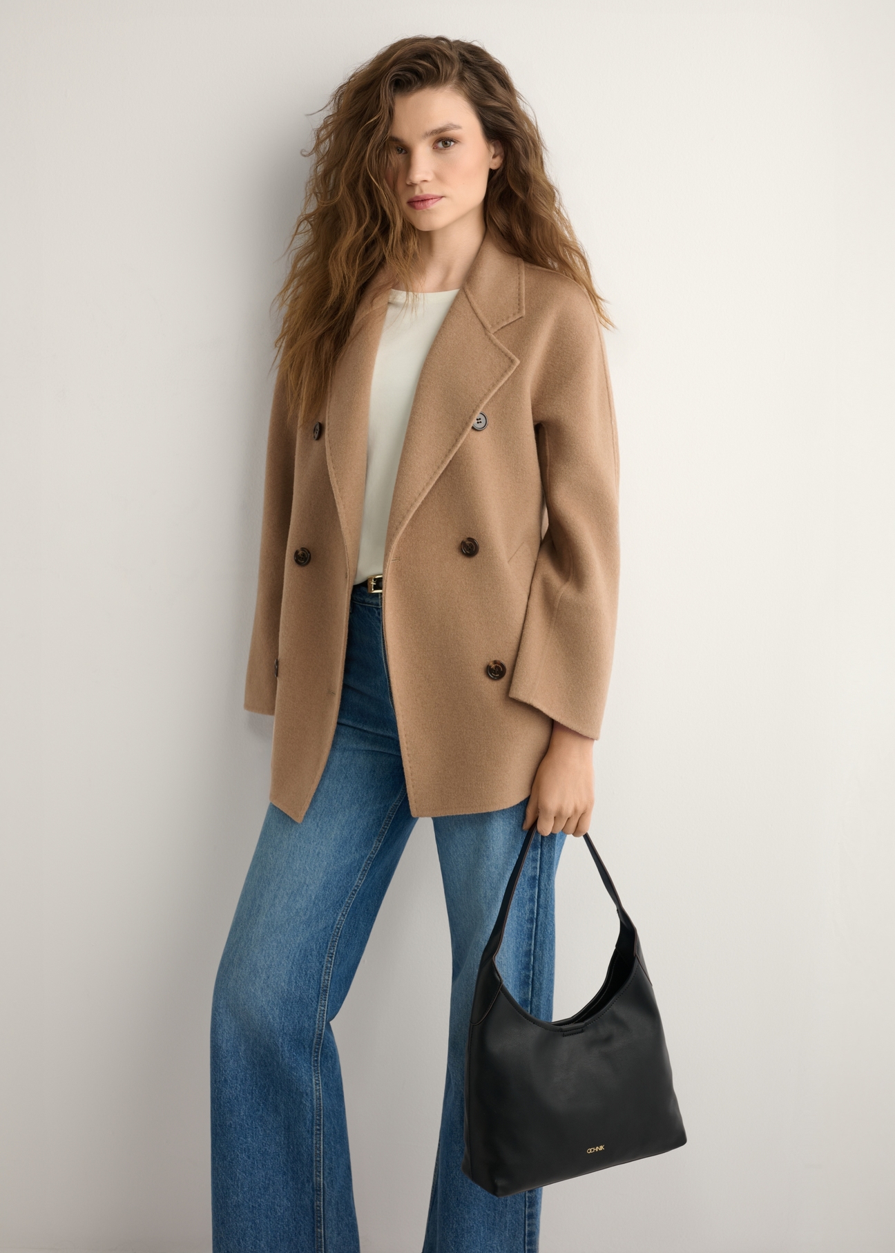 Čierna stredne veľká dámska kabelka TOREC-1200-99(W26), pohľad na produkt v ruke modelky. Viditeľná polovica siluety.