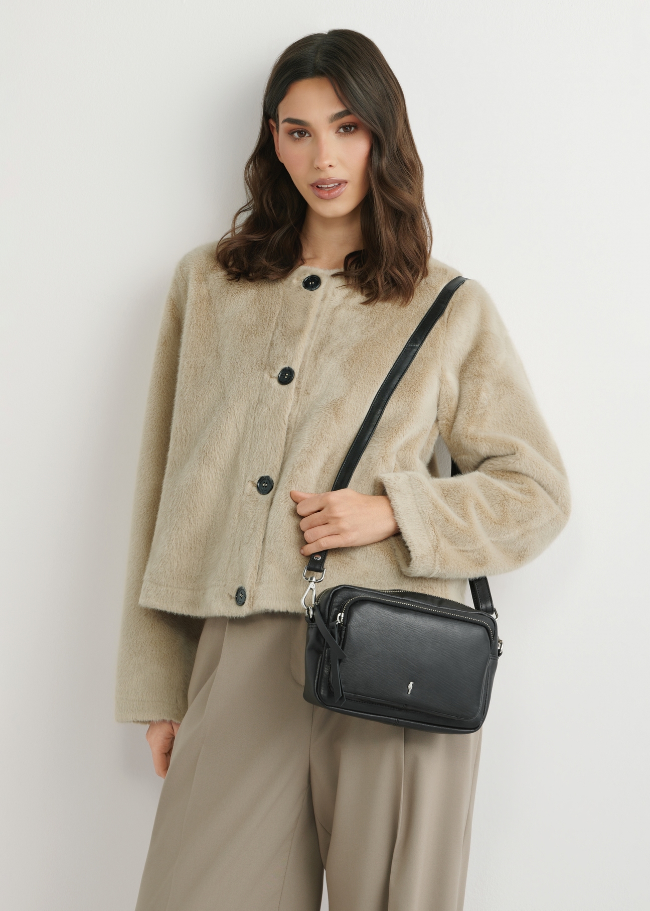 Malá čierna kožená dámska kabelka TORES-1023A-99(W26), pohľad spredu na produkt na ramene modelky. Viditeľná polovica siluety.