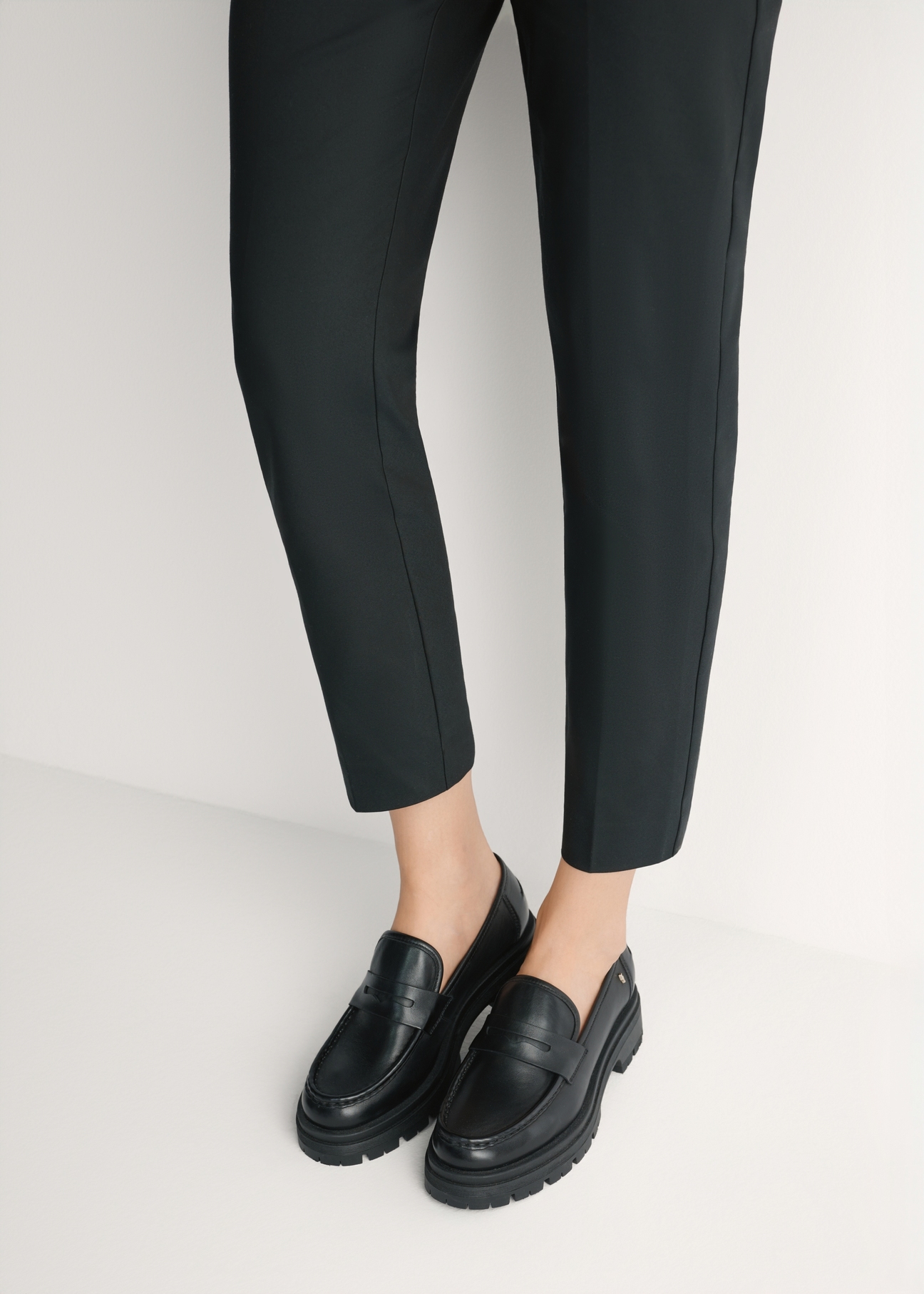 Dámske čierne kožené mokasíny BUTYD-1069-99(W26) - pohľad spredu na výrobok, na modelke, na svetlom pozadí. Viditeľná silueta po kolená.