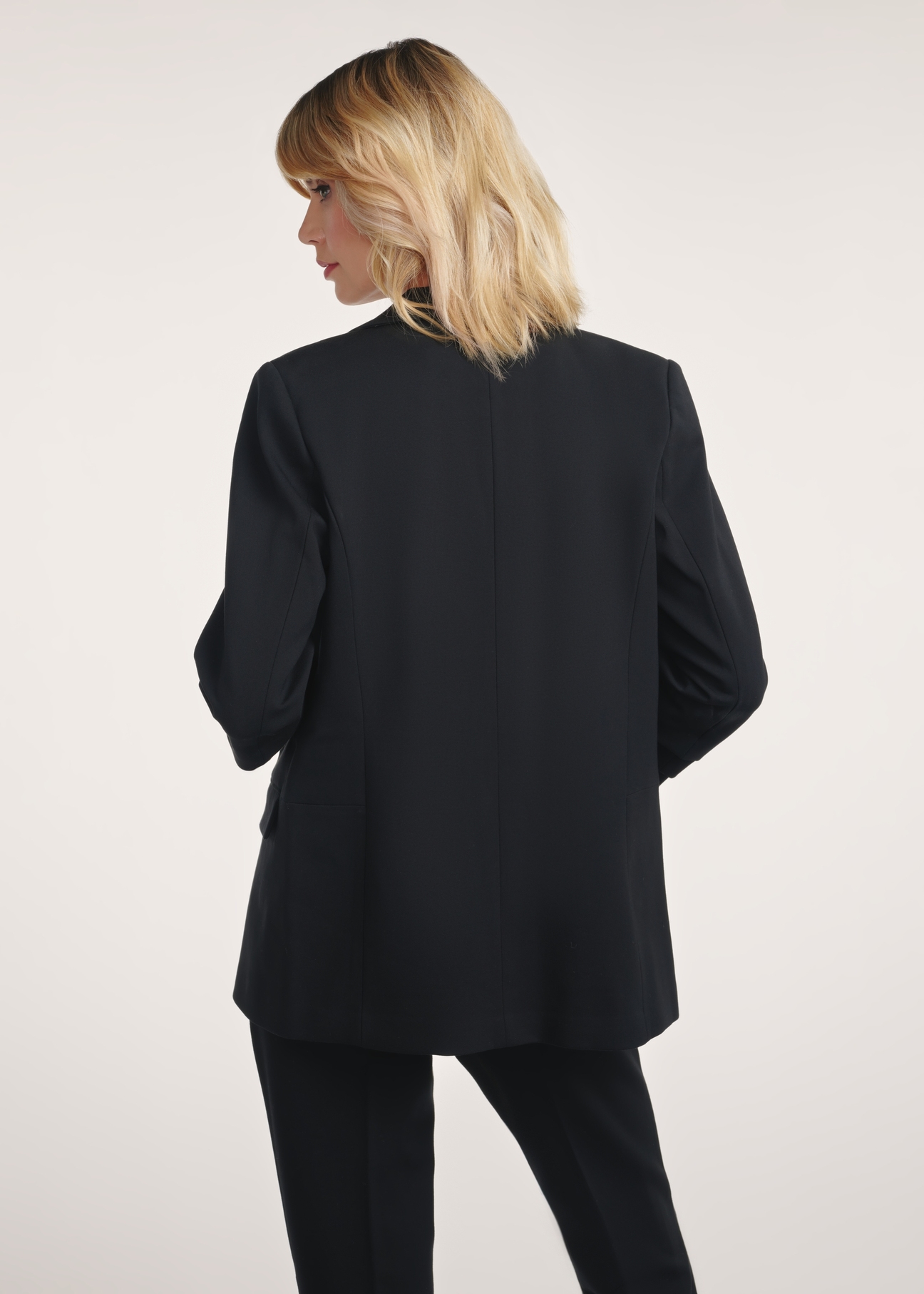 Čierna dámska bunda bez zapínania ZAKDT-0034-99(Z24) - pohľad na produkt zozadu na modelke na bielom pozadí. Je viditeľná polovica siluety.