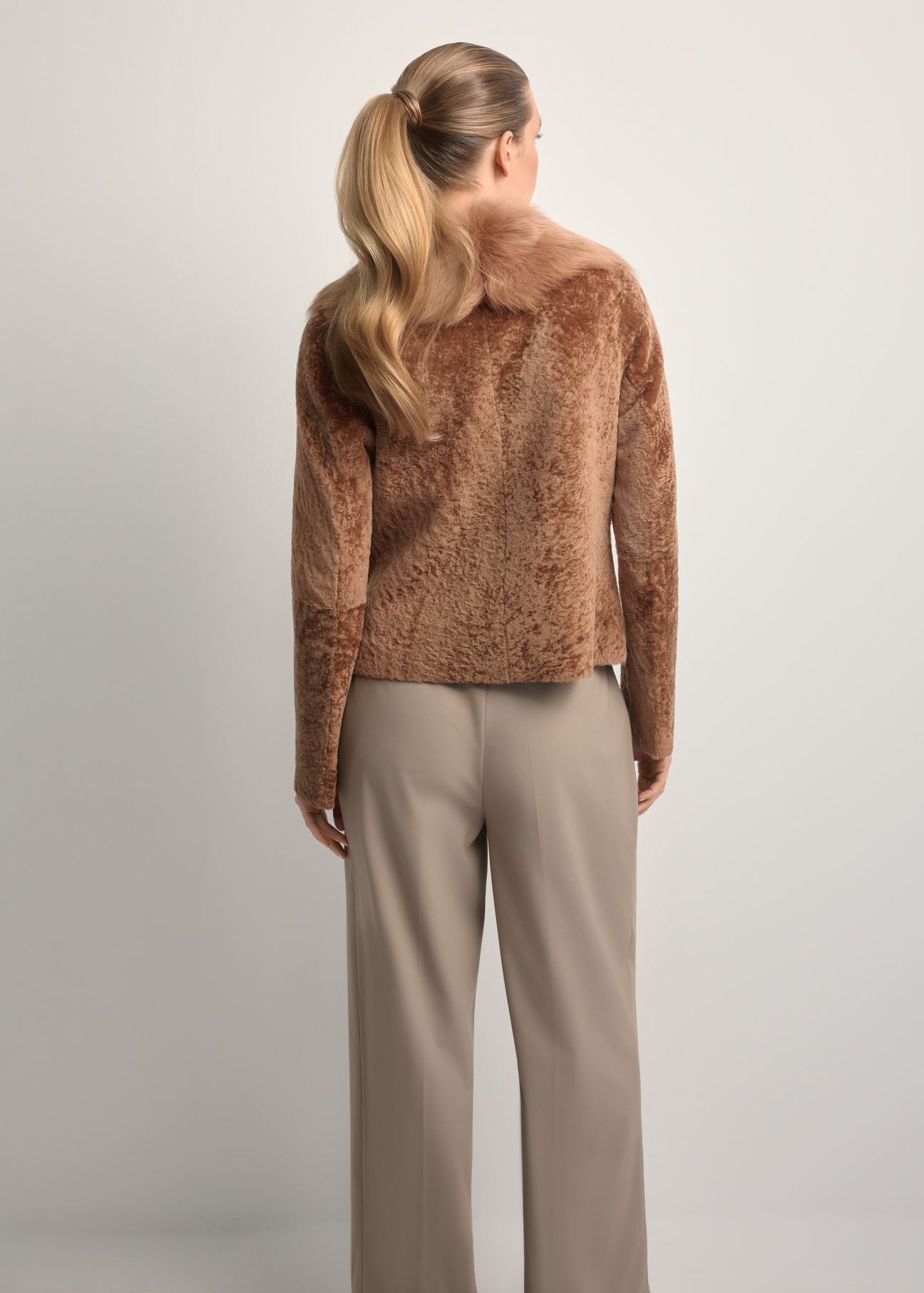 Dámsky kožený kabát z ovčej kože ťavej farby KOZDS-0095-3099(Z25), pohľad na modelku zozadu. Viditeľná polovica siluety.