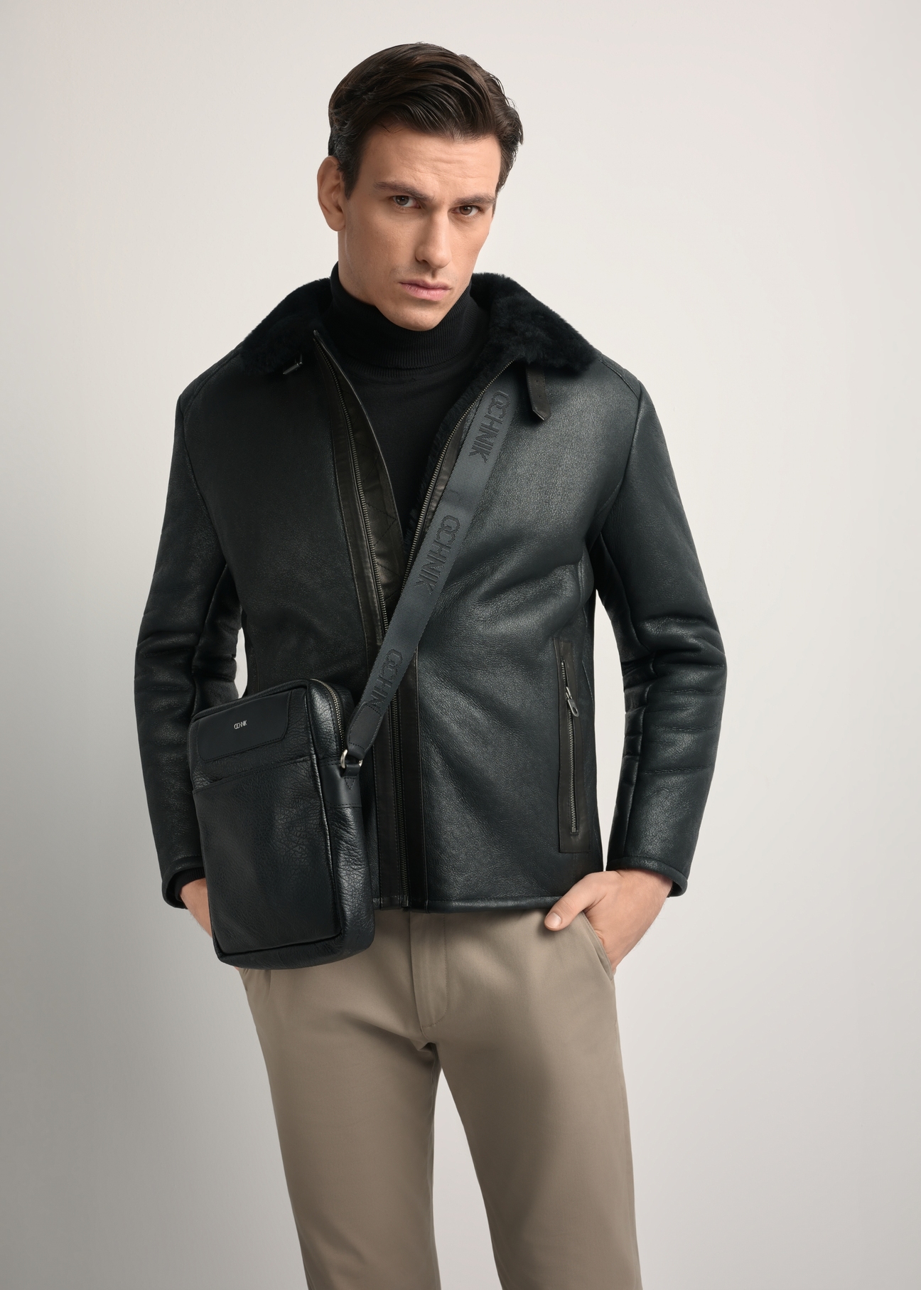 Čierna kožená pánska taška s logom TORMS-0297A-99(Z25) - diagonálny pohľad na produkt, modelovaný na bielom pozadí. Viditeľná silueta po kolená.