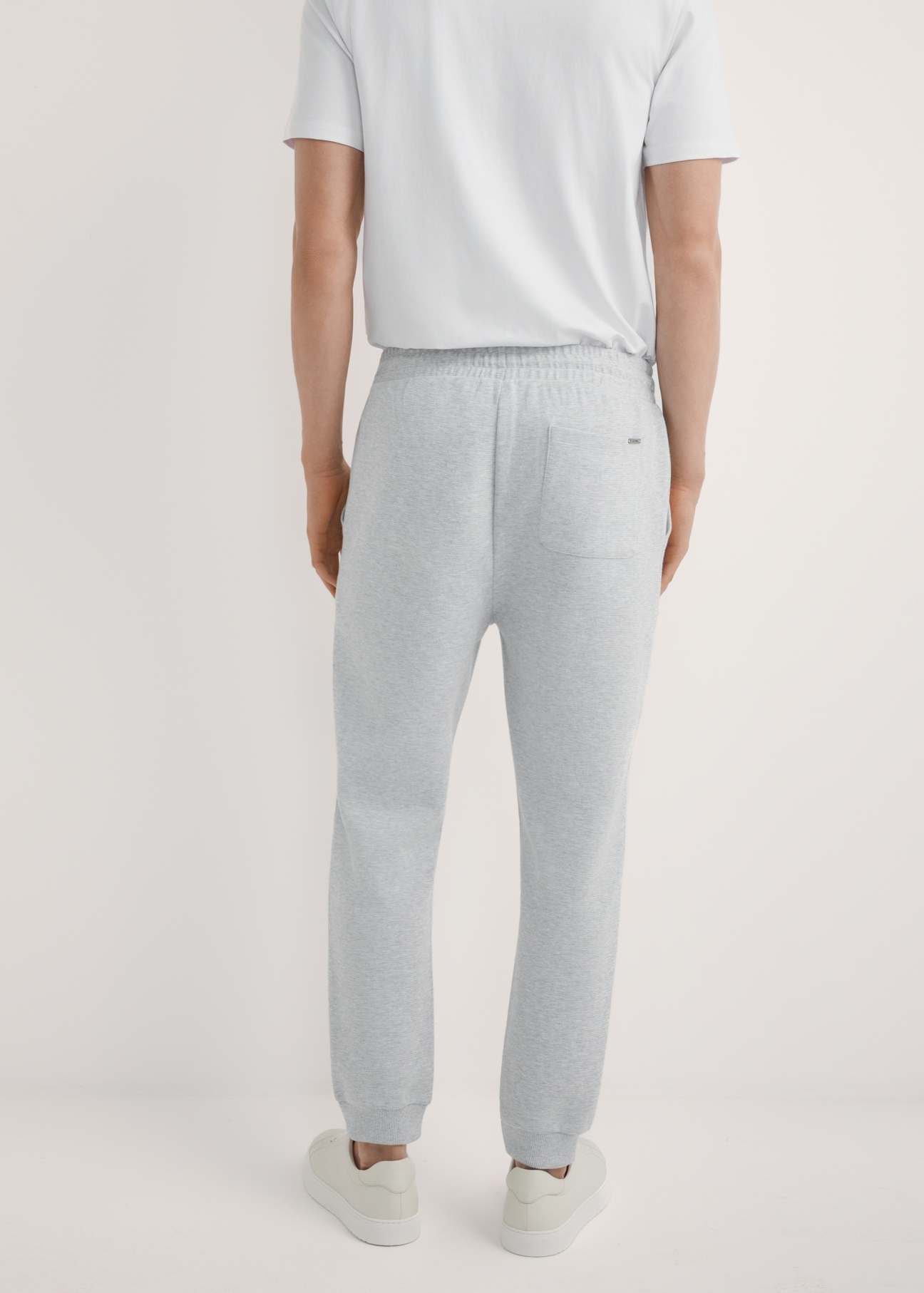 Pánske sivé tepláky SPOMT-0116-9A(W26), pohľad na produkt zozadu na modeli. Viditeľná polovica siluety.