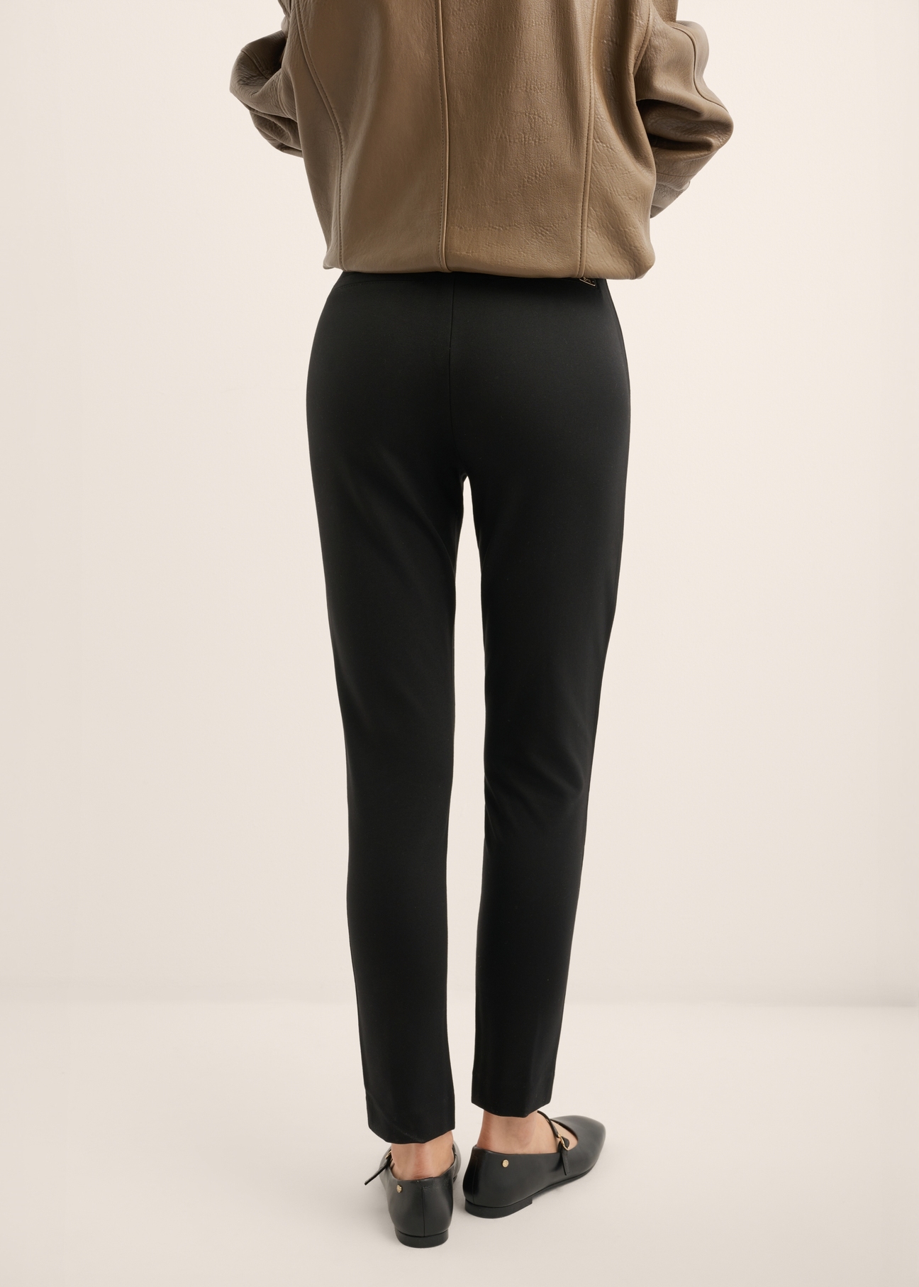 Čierne priliehavé dámske nohavice SPODT-0096-99(Z25), pohľad na modelku zozadu. Viditeľná polovica siluety.