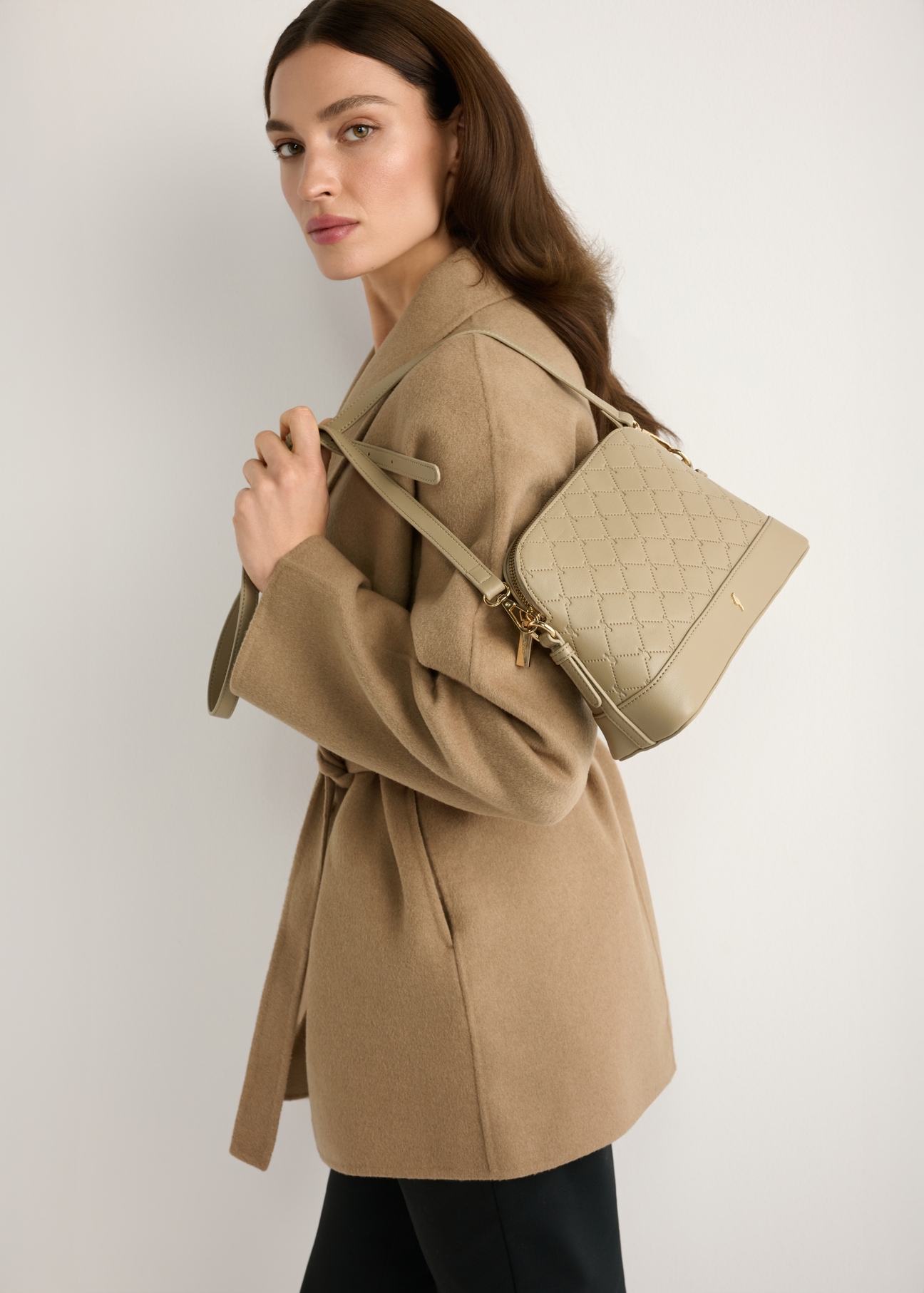 Béžová dámska kabelka s monogramom TOREC-1180-1P(W26) - mierne diagonálny pohľad na produkt, ktorý drží modelka, na svetlom pozadí. Viditeľná je polovica siluety.