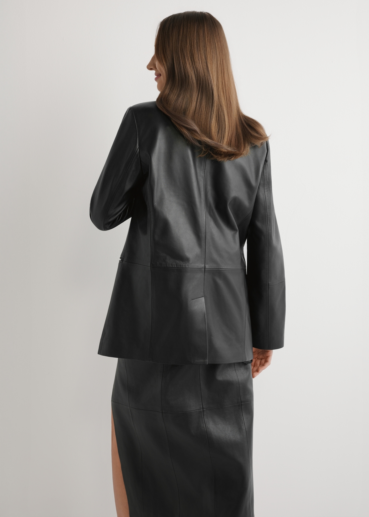 Dámska čierna kožená bunda KURDS-0606-99(W26) - pohľad na modelku zozadu, na svetlom pozadí. Viditeľná silueta po kolená.