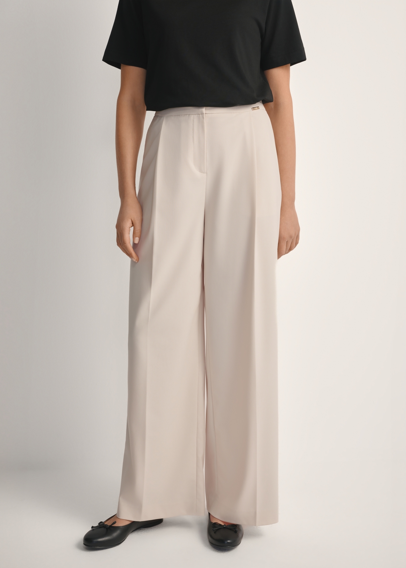 Svetlobéžové dámske nohavice SPODT-0119-1A(W26), pohľad spredu na výrobok na modelke. Viditeľná polovica siluety.