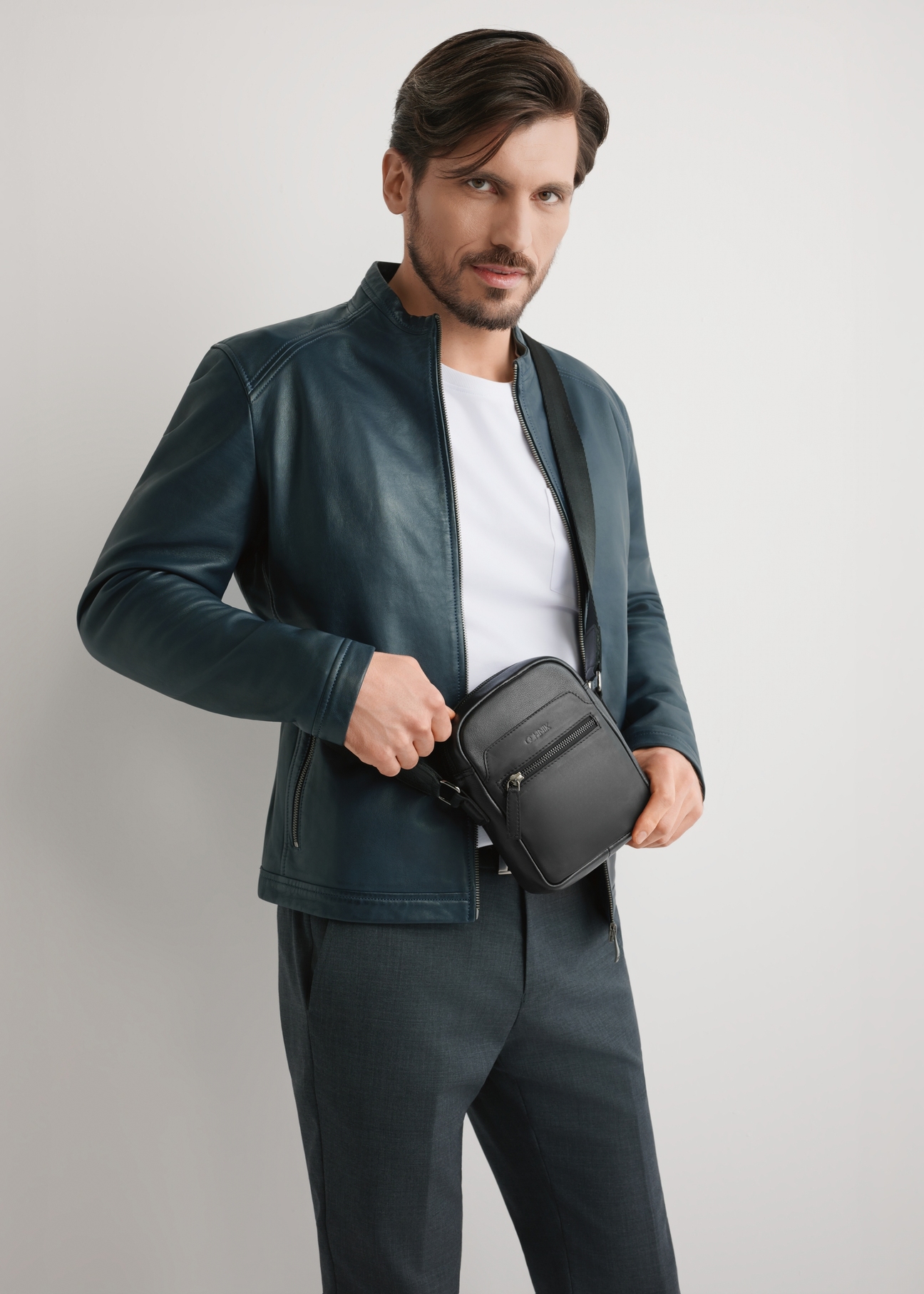 Čierna malá kožená pánska taška TORMS-0498-99(W26) - pohľad spredu na produkt, na modelke, na svetlom pozadí. Viditeľná silueta po kolená.