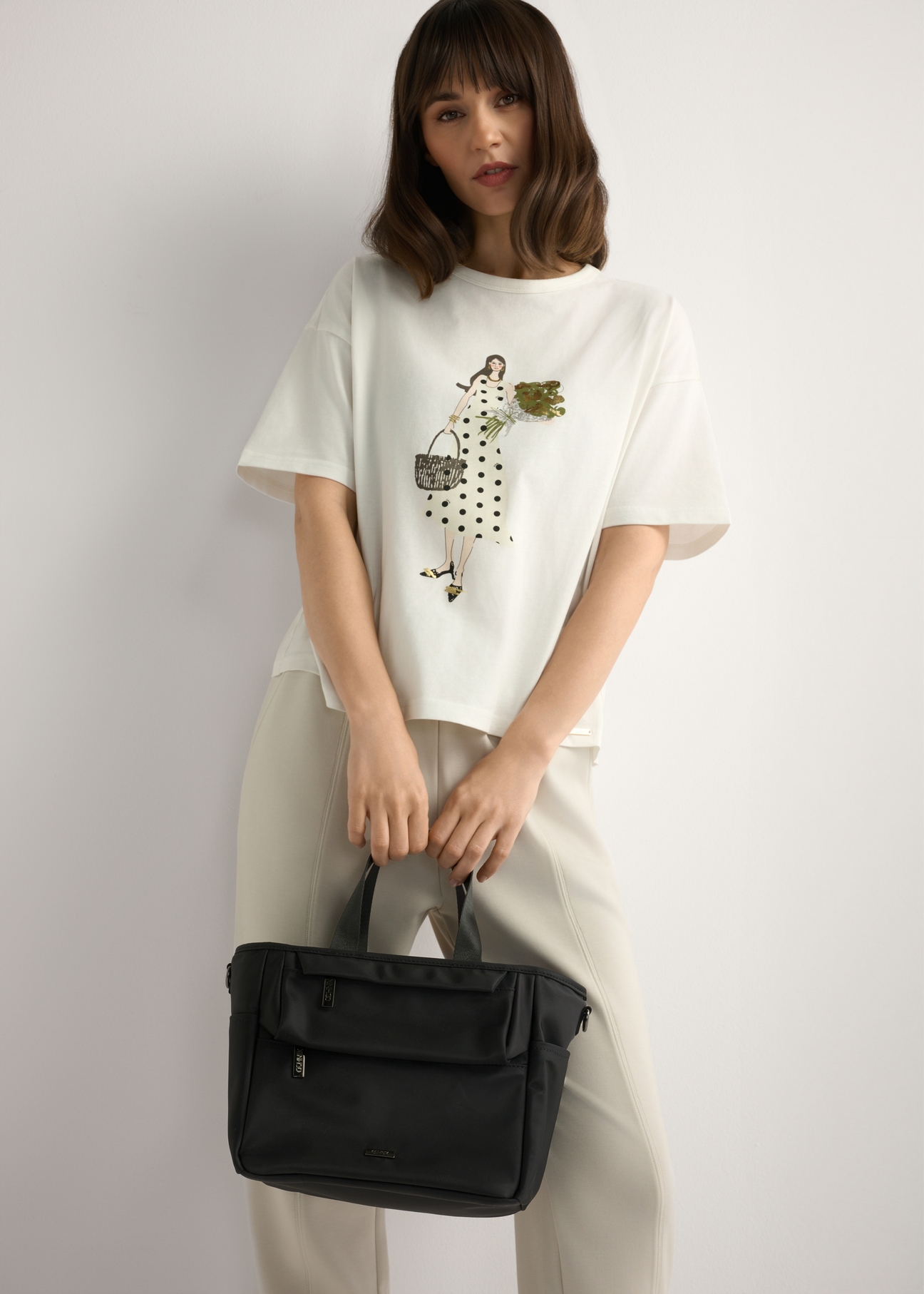 Čierna obedárová taška TOREN-0346-99(W26) - pohľad na produkt držaný v ruke modelky na svetlom pozadí. Viditeľná silueta po kolená.